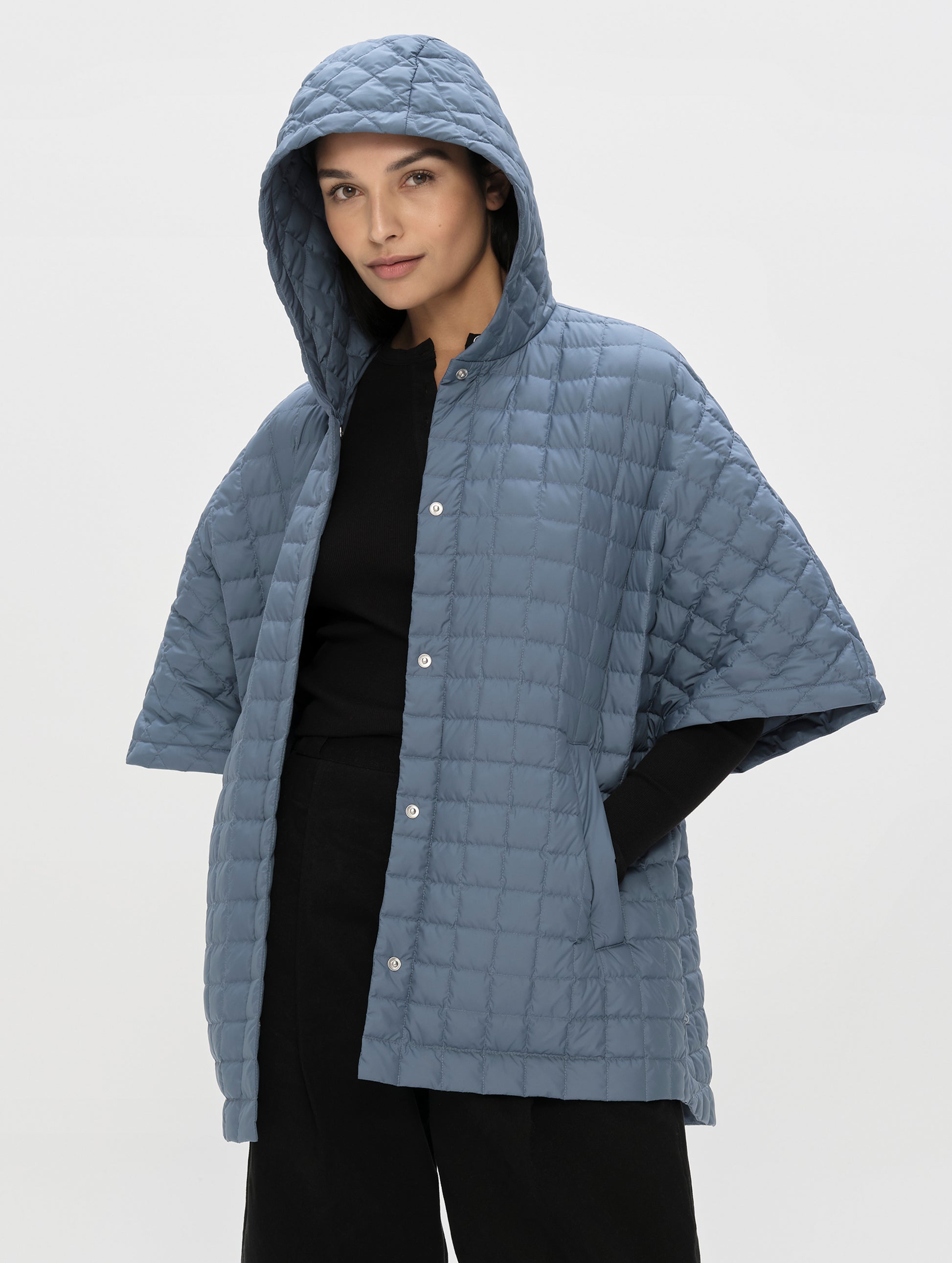 Front, angled upper-body view of woman with hood up wearing the Bardo Hooded Poncho in Portal Blue from AETHER Apparel.