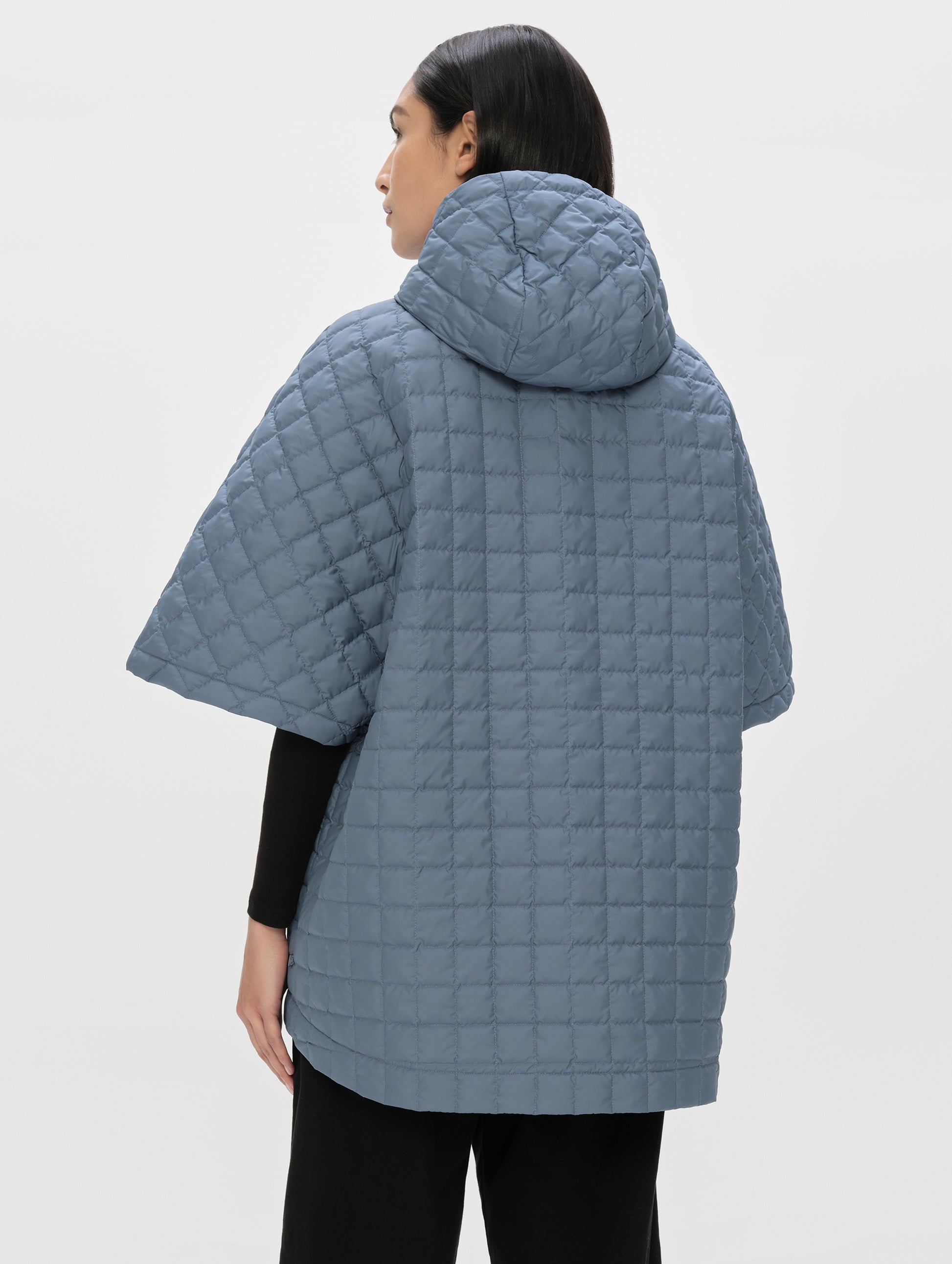 Rear angled upper-body view of woman wearing the Bardo Hooded Poncho in Portal Blue from AETHER Apparel.