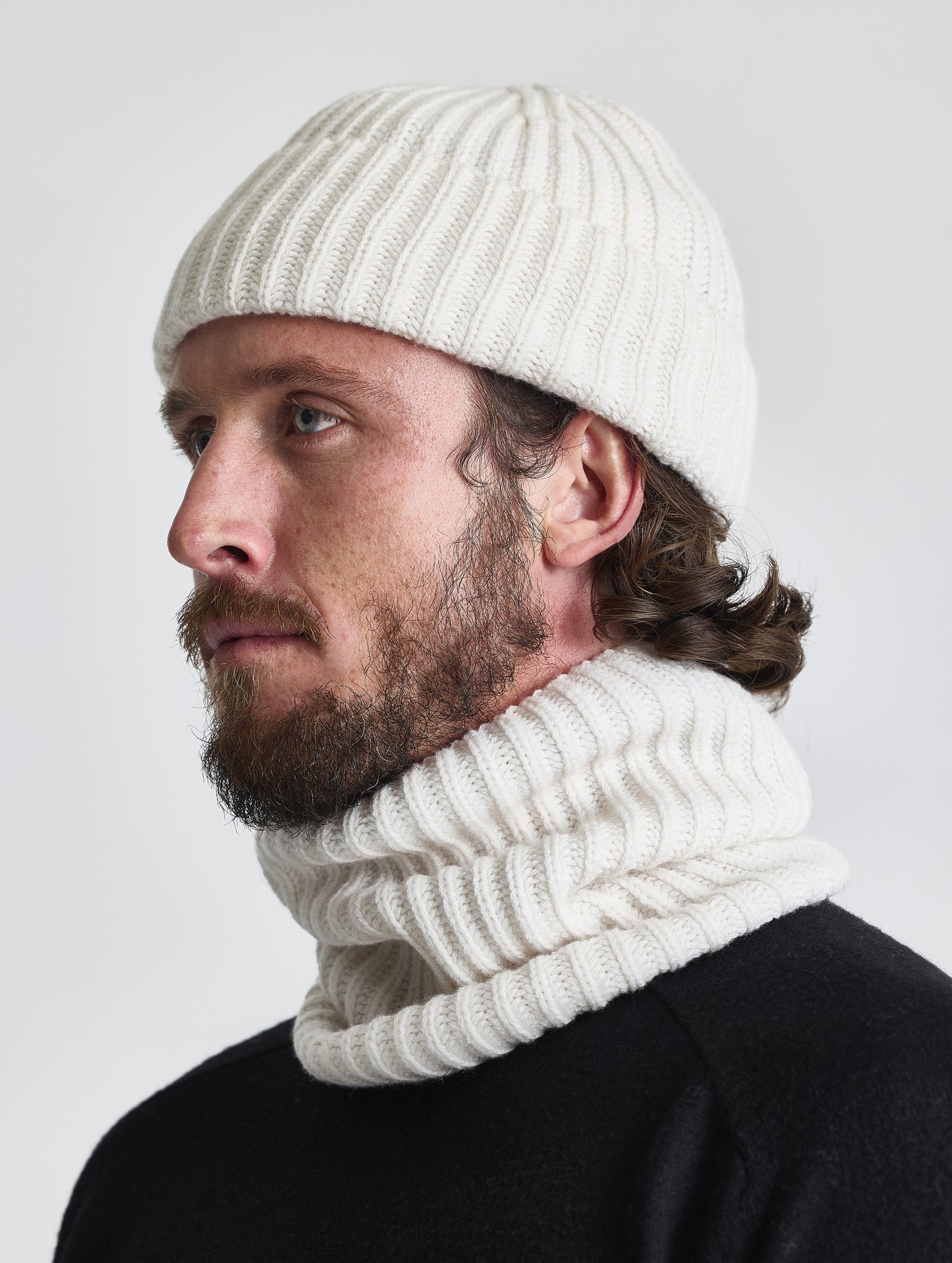 Side profile view of man wearing the Cashmere Hat and the Cashmere Neck Gaiter in Winter White from AETHER Apparel. 