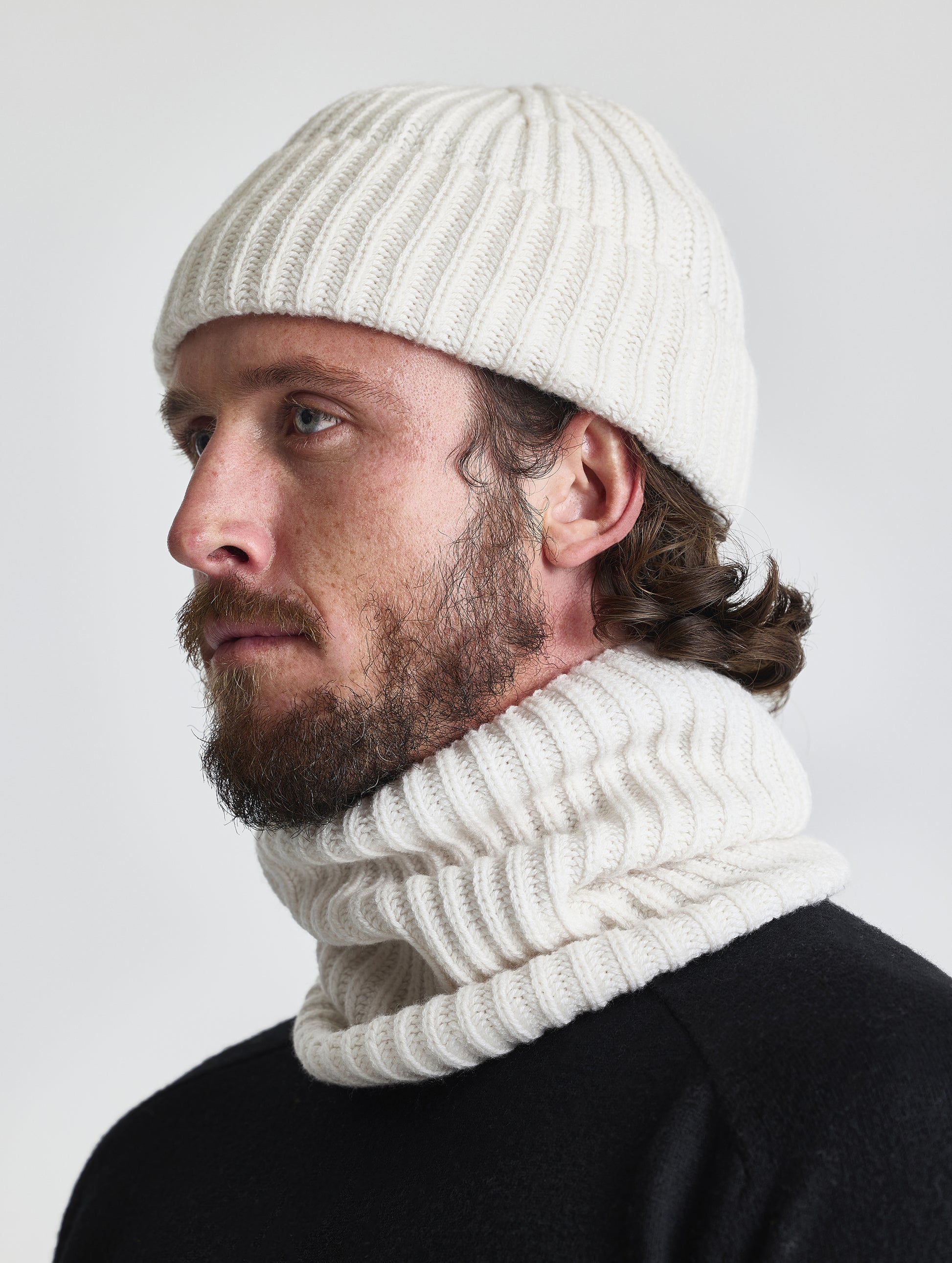 Side profile view of man wearing the Cashmere Hat and the Cashmere Neck Gaiter in Winter White from AETHER Apparel. 