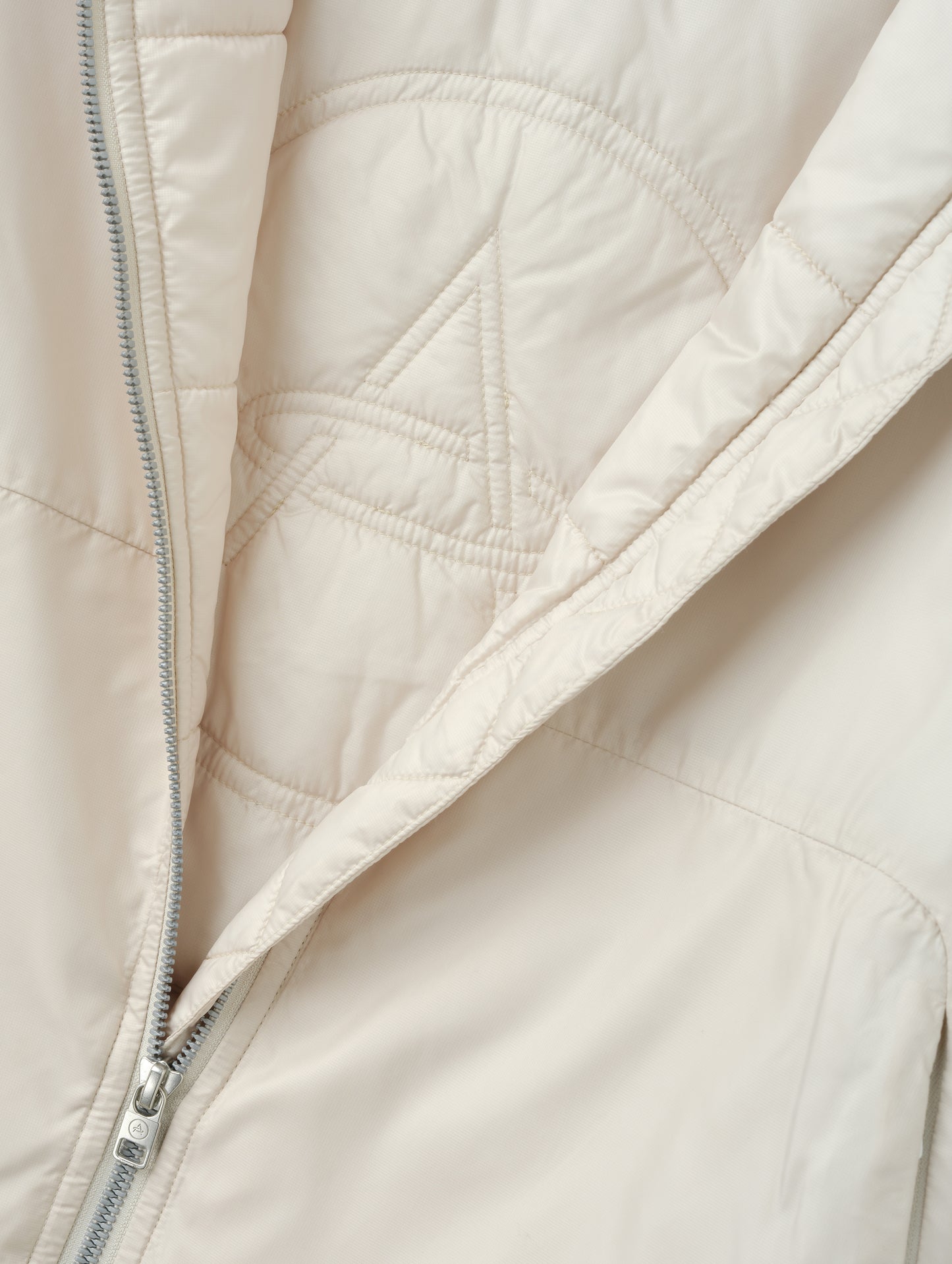 Closeup detailed view of the custom AETHER logo quilting on the interior of the Celeste Eco Insulated Hoodie in Bone from AETHER Apparel.
