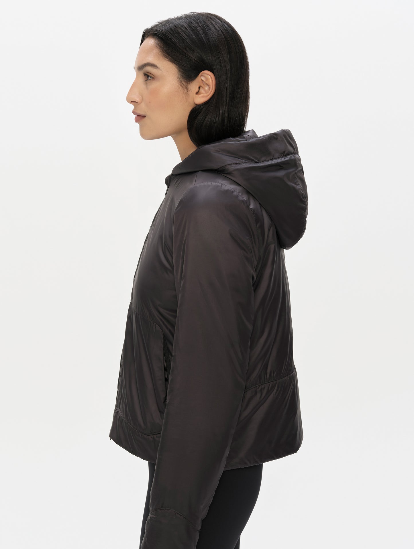 Side profile upper-body view of woman wearing the Celeste Eco Insulated Hoodie in Onyx Black from AETHER Apparel.