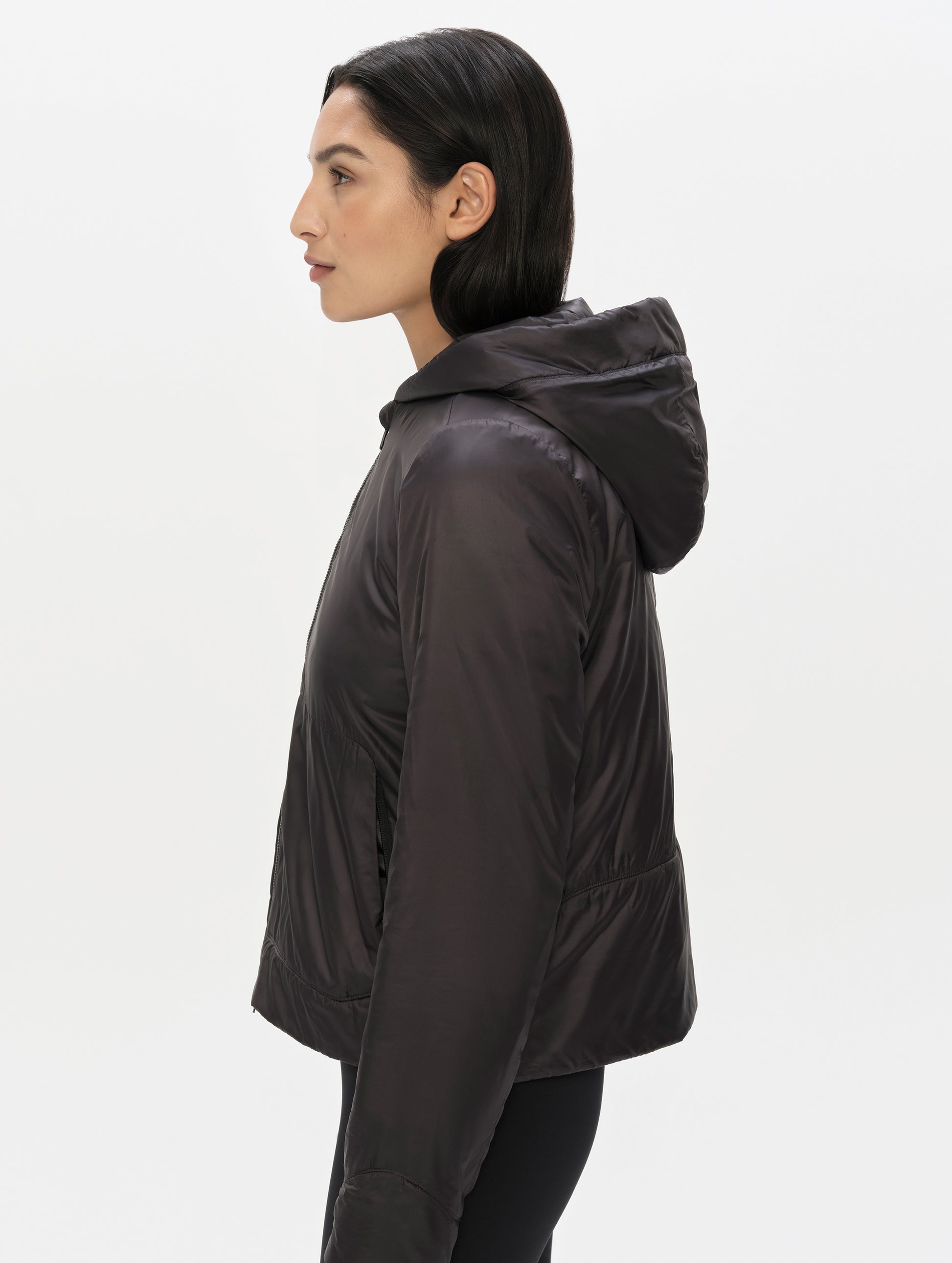 Side profile upper-body view of woman wearing the Celeste Eco Insulated Hoodie in Onyx Black from AETHER Apparel.