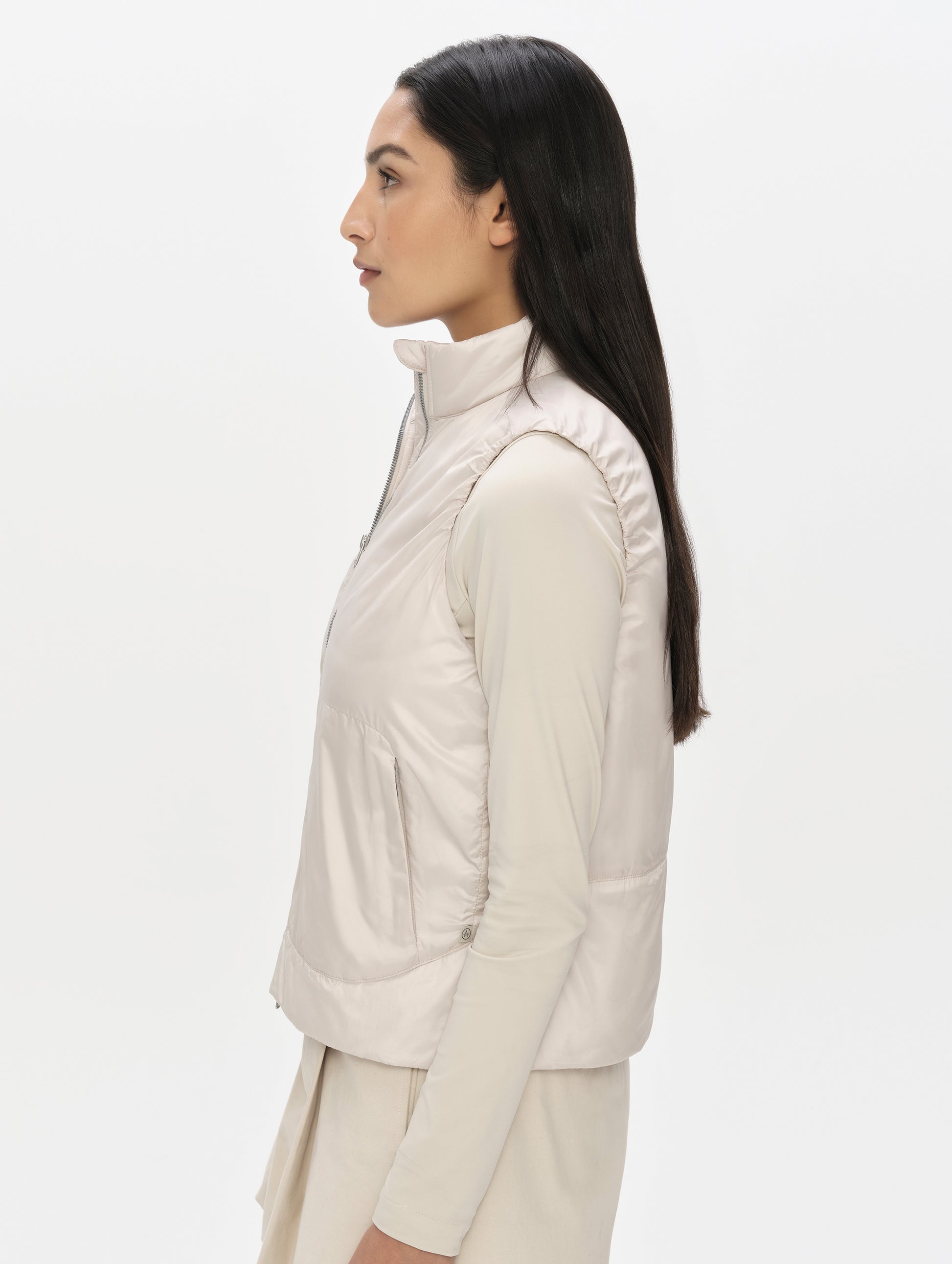 Side profile, upper-body view of woman wearing the Celeste Eco Insulated Vest in Bone from AETHER Apparel.
