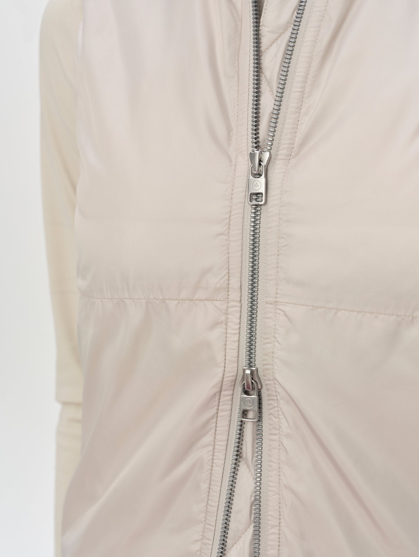 Closeup detailed view of the two-way center-front zipper on the Celeste Eco Insulated Vest in Bone from AETHER Apparel.