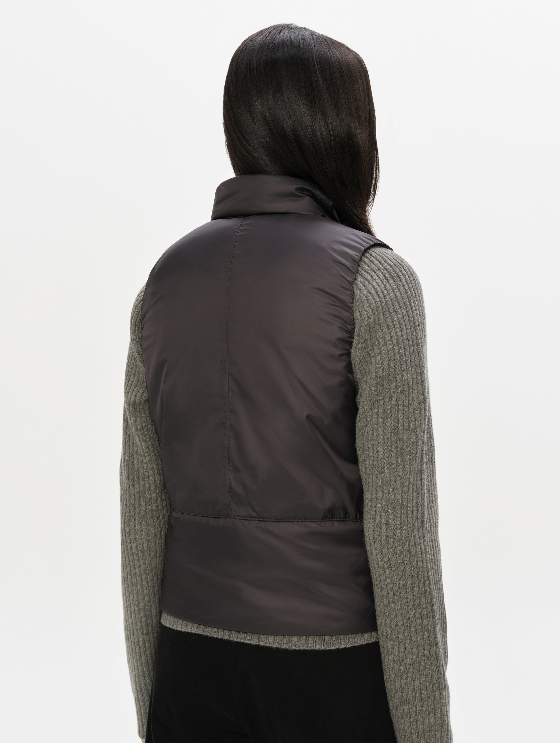 Rear, angled upper-body view of woman wearing the Celeste Eco Insulated Vest in Onyx Black from AETHER Apparel.