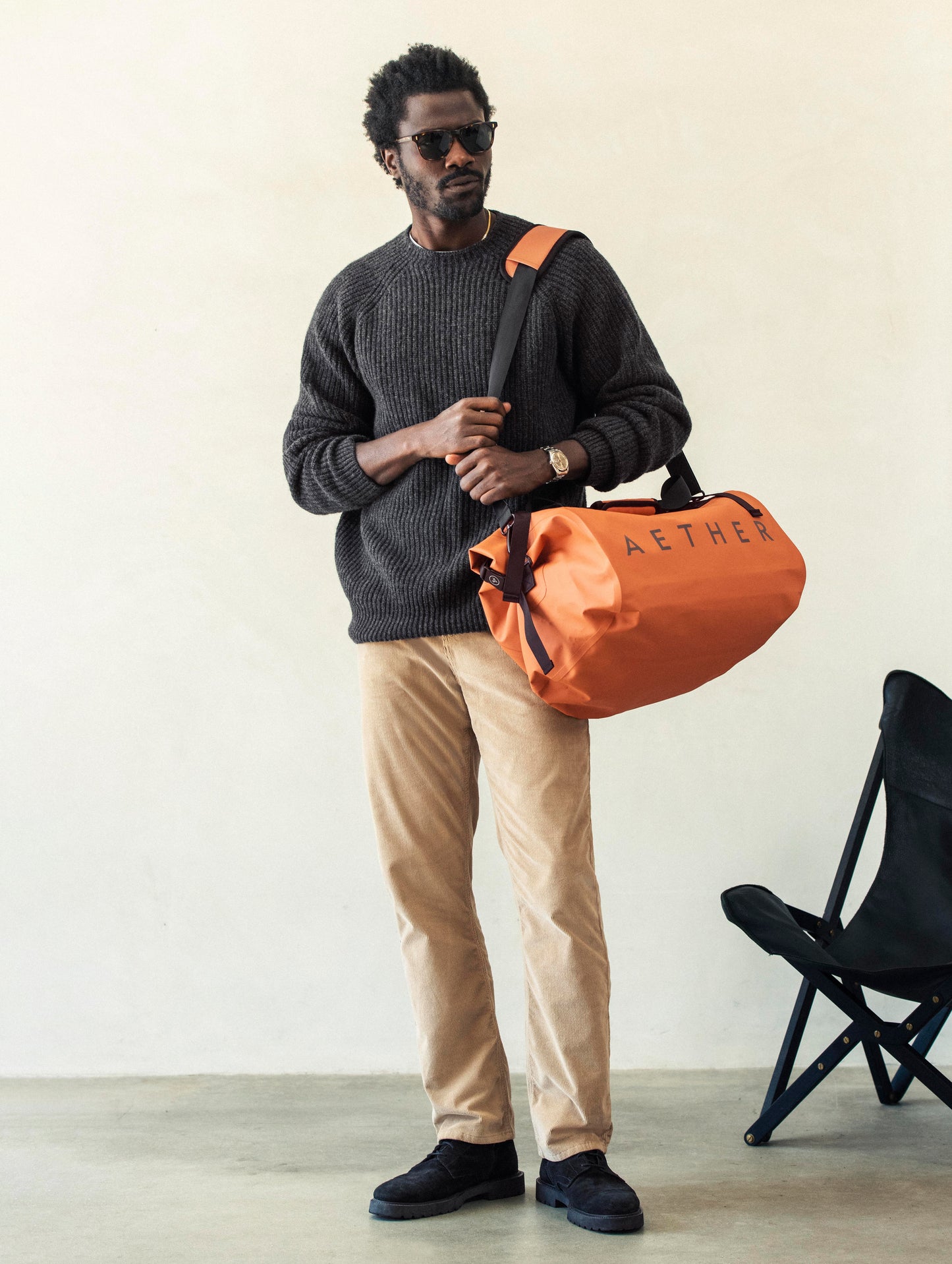 Front angled full-body view of man carrying Excursion Duffle Bag 45L in Autumn Orange from AETHER Apparel over shoulder. 