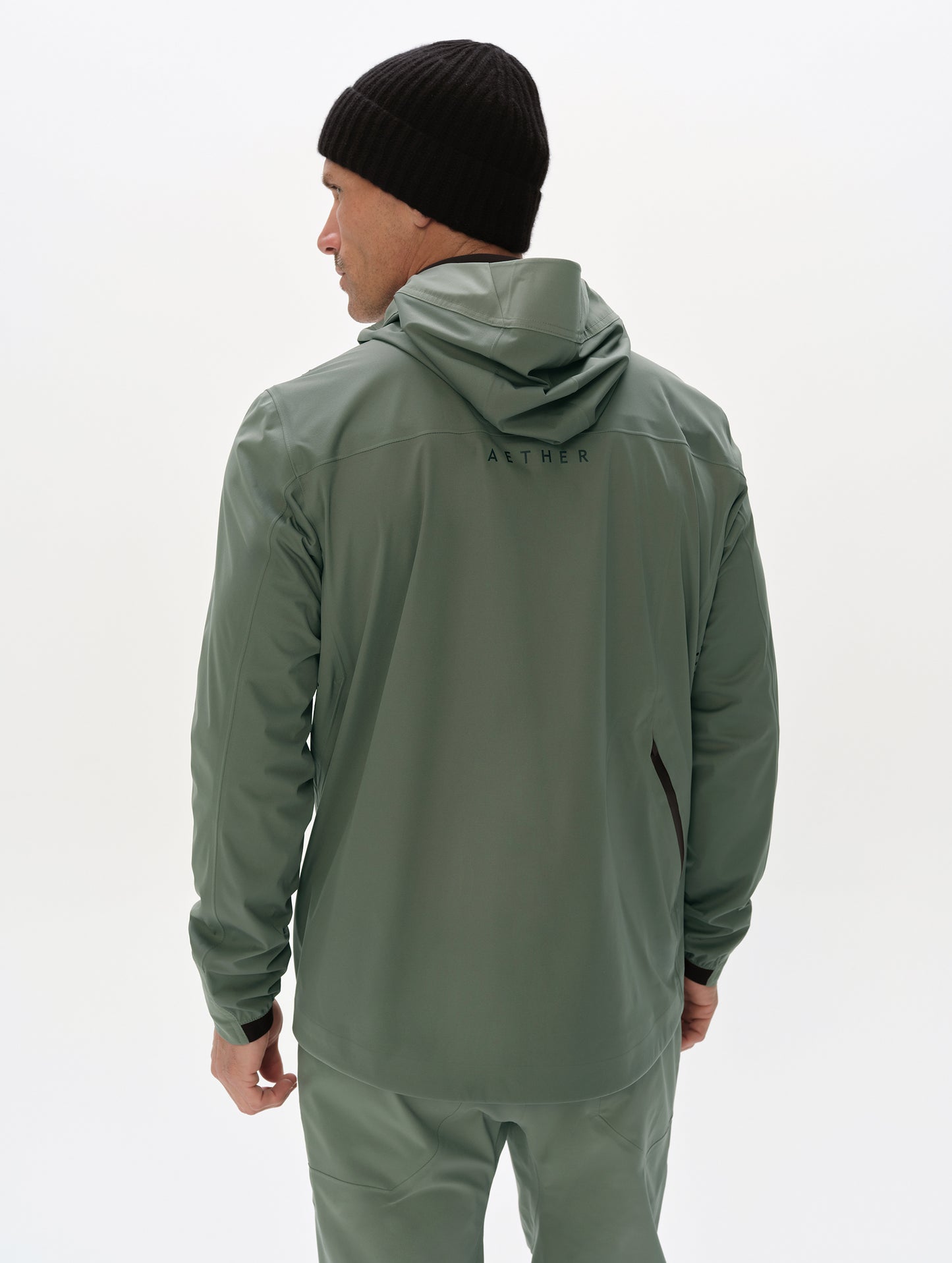 Rear, upper-body view of man wearing the Frontier Hooded Shell Jacket in Gunmetal from AETHER Apparel.
