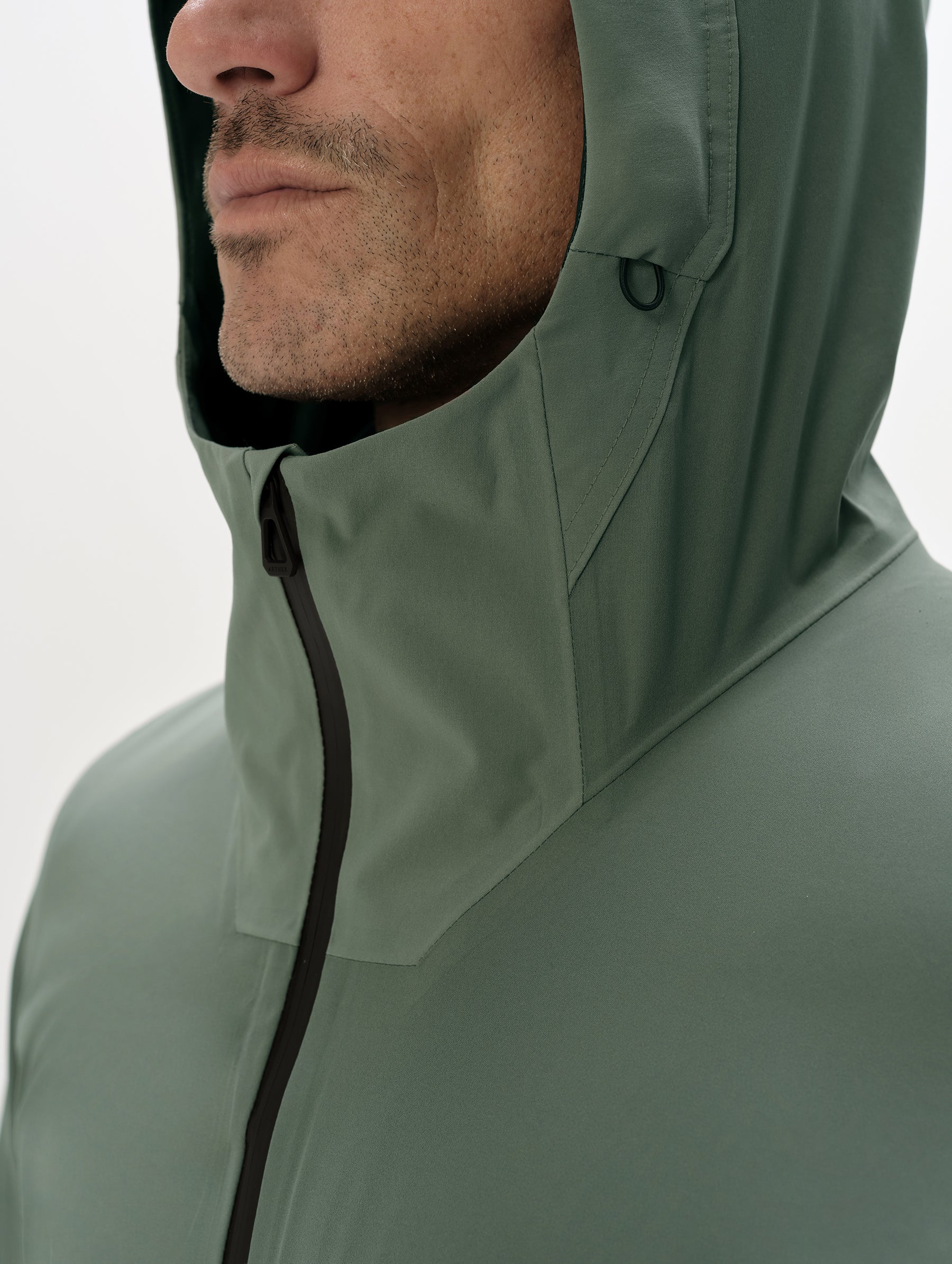 Closeup detailed view of the multi-piece hood and center-front zipper closure on the Frontier Hooded Shell Jacket in Gunmetal from AETHER Apparel.
