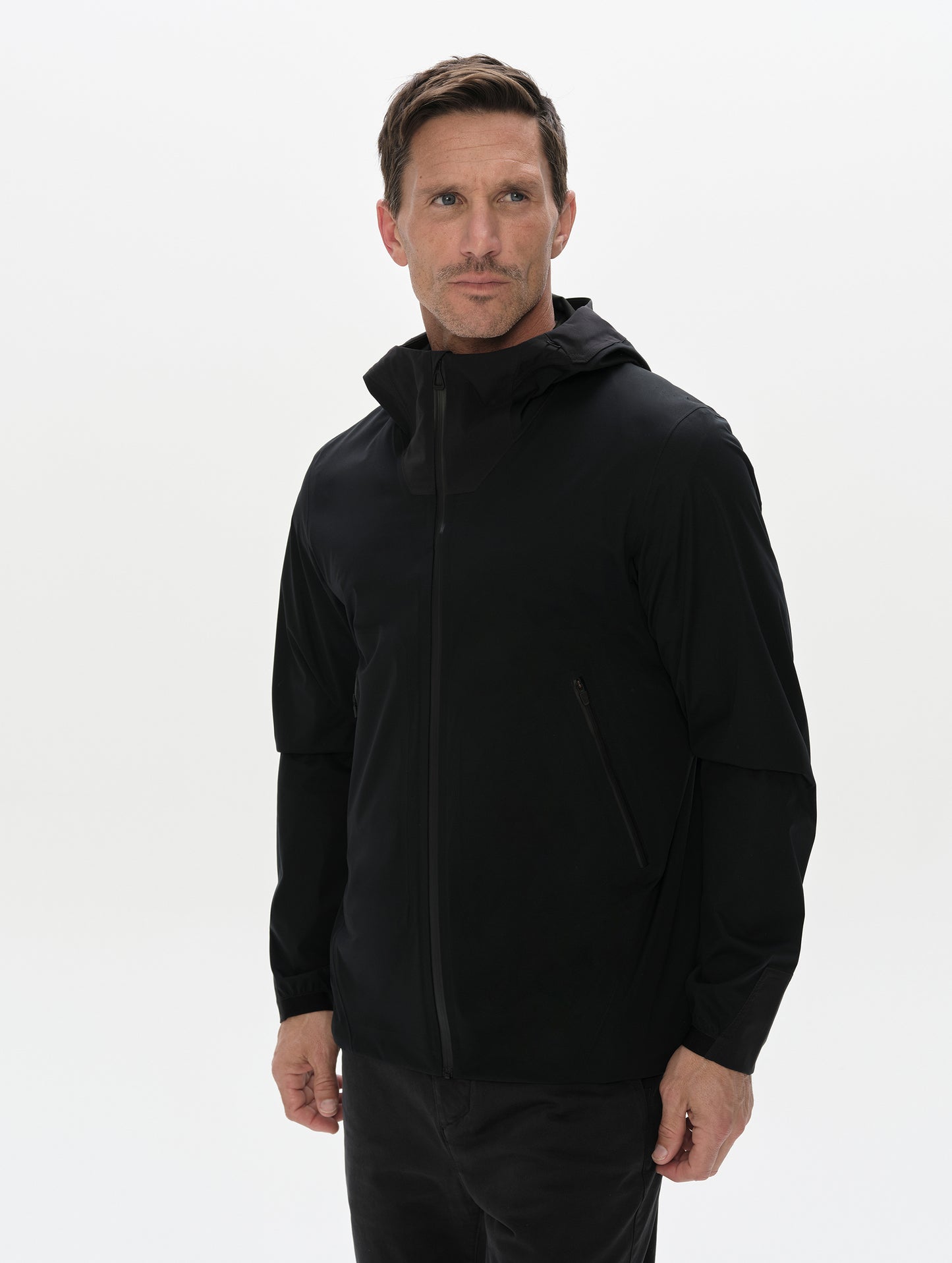 Front, 3/4 upper-body view of man wearing the Frontier Hooded Shell Jacket in Onyx Black from AETHER Apparel.