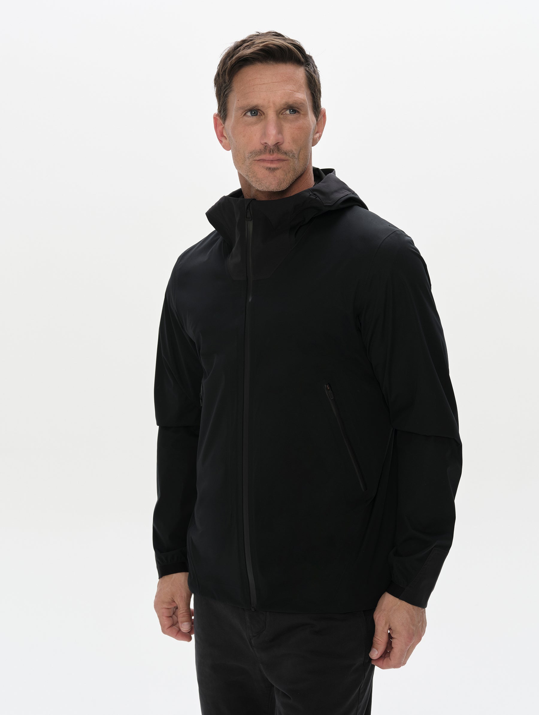Front, 3/4 upper-body view of man wearing the Frontier Hooded Shell Jacket in Onyx Black from AETHER Apparel.