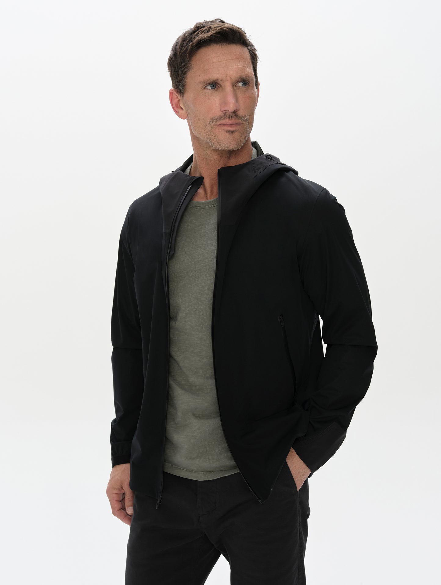 Front, upper-body view of man wearing the Frontier Hooded Shell Jacket in Onyx Black from AETHER Apparel.