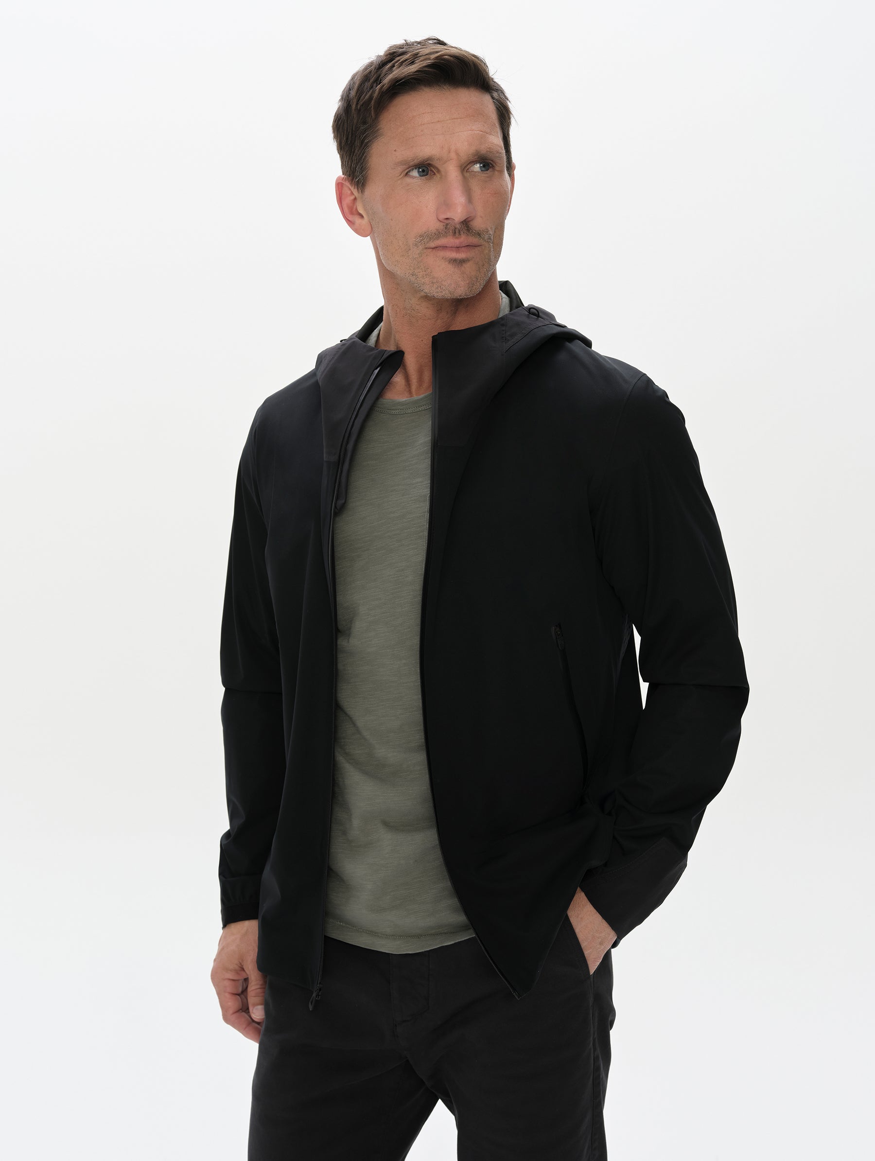 Front, upper-body view of man wearing the Frontier Hooded Shell Jacket in Onyx Black from AETHER Apparel.