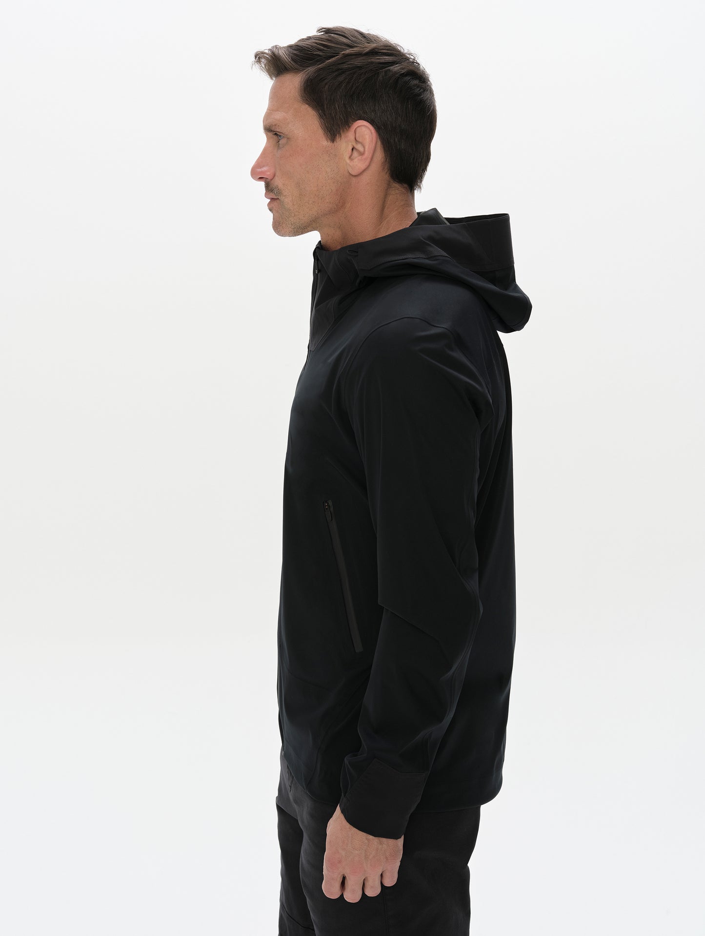 Side profile, upper-body view of man wearing the Frontier Hooded Shell Jacket in Onyx Black from AETHER Apparel.