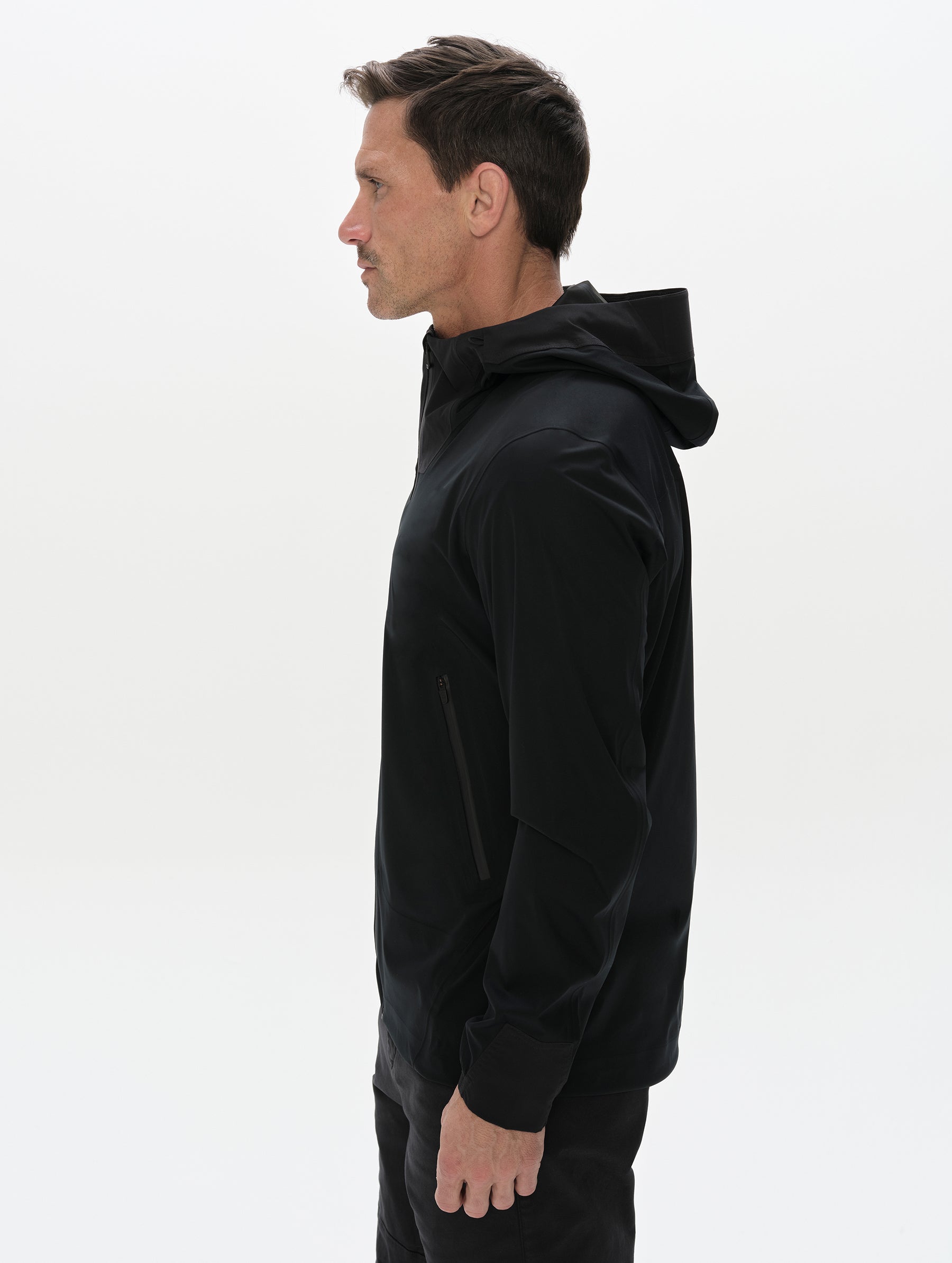 Side profile, upper-body view of man wearing the Frontier Hooded Shell Jacket in Onyx Black from AETHER Apparel.