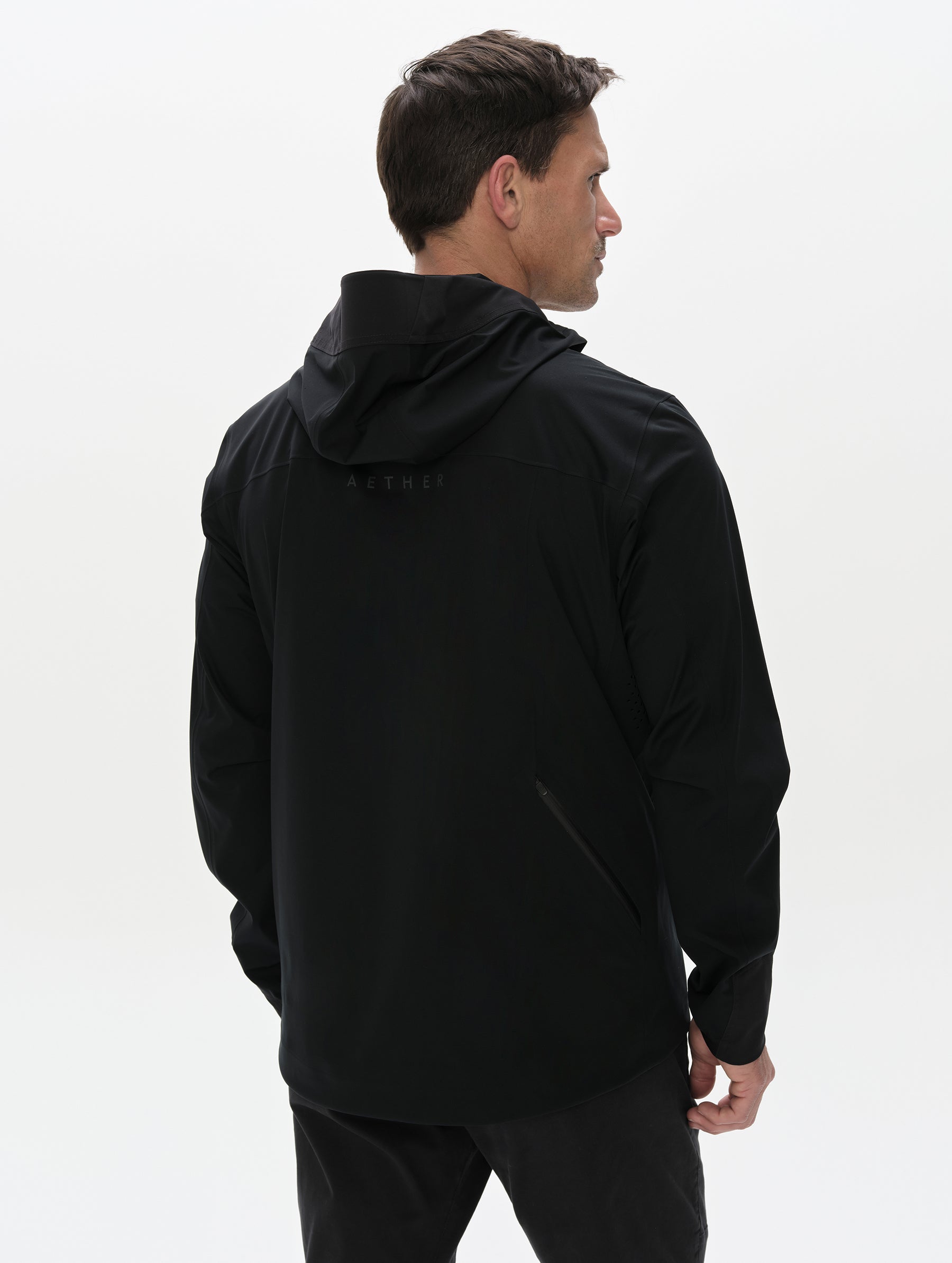 Rear, upper-body view of man wearing the Frontier Hooded Shell Jacket in Onyx Black from AETHER Apparel.
