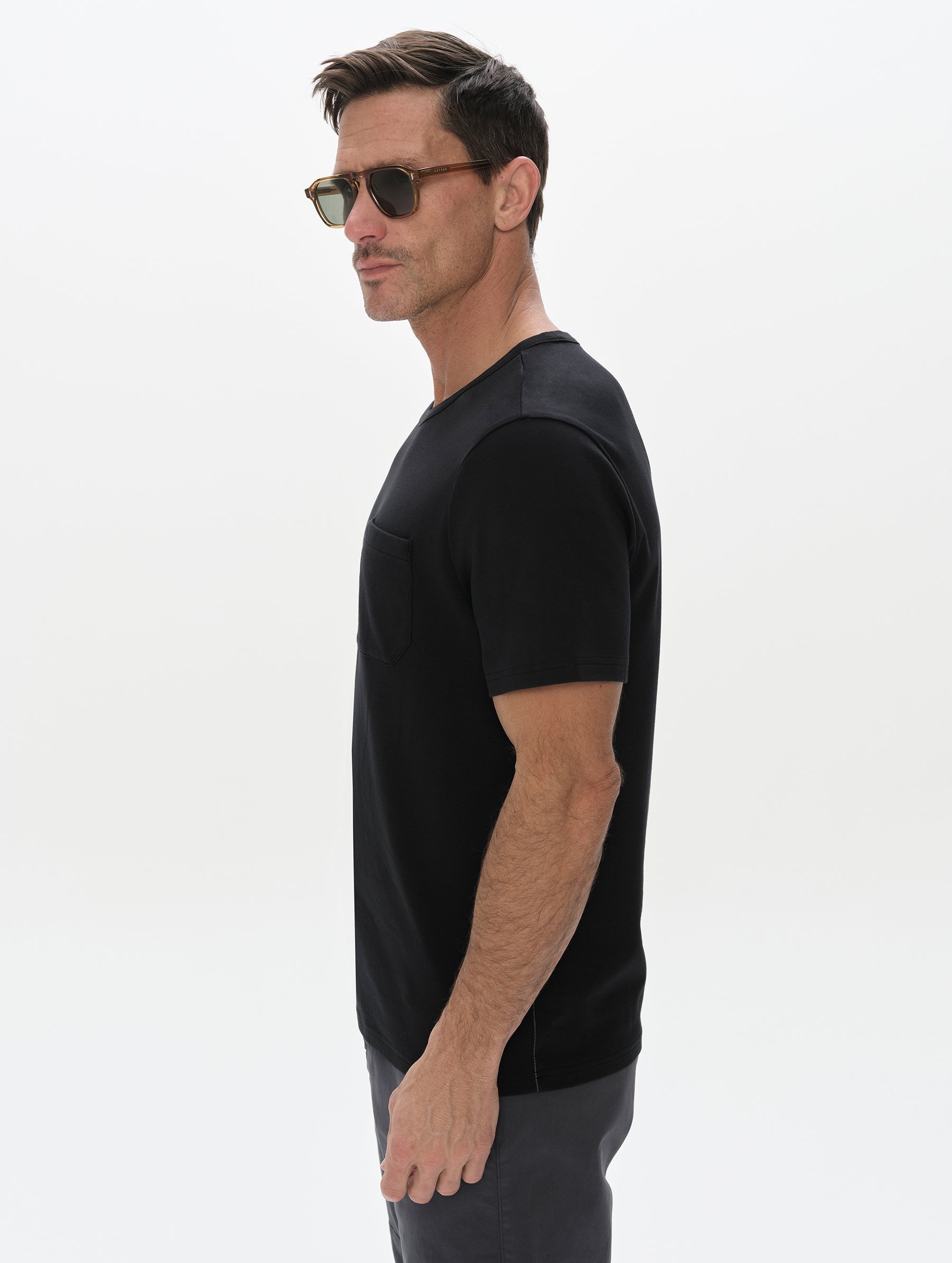 Side profile, upper-body view of man wearing the Harlow Premium Tee in Onyx Black from AETHER Apparel.
