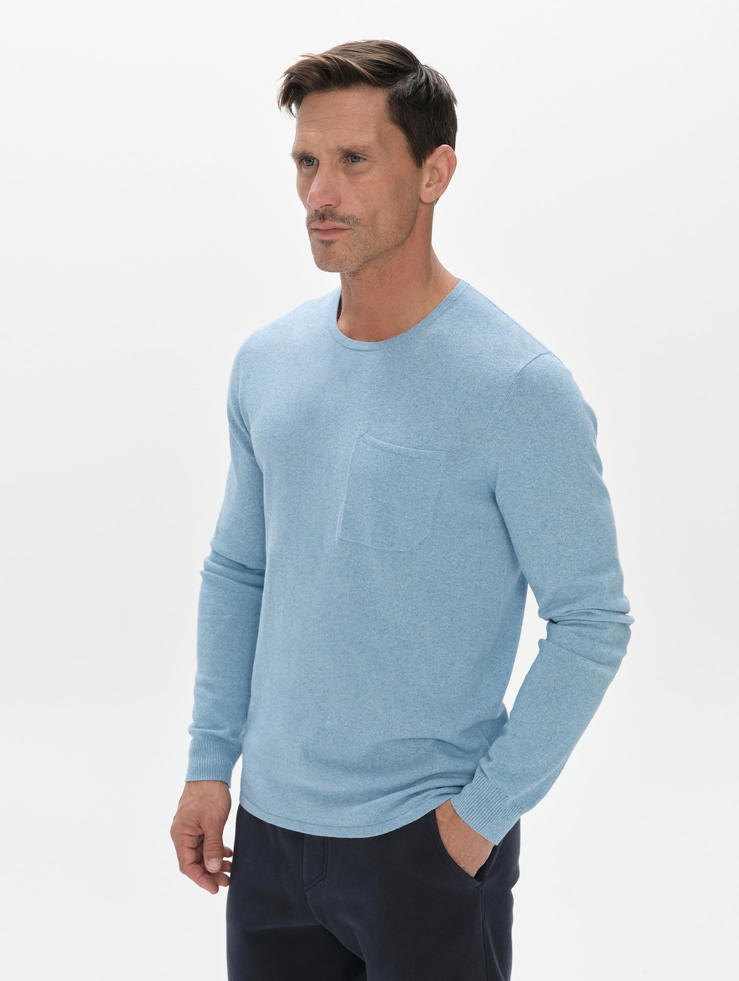 Front, 3/4, upper-body view of the man wearing the Aero Crewneck Sweater 2.0 in Cloud Blue from AETHER Apparel.