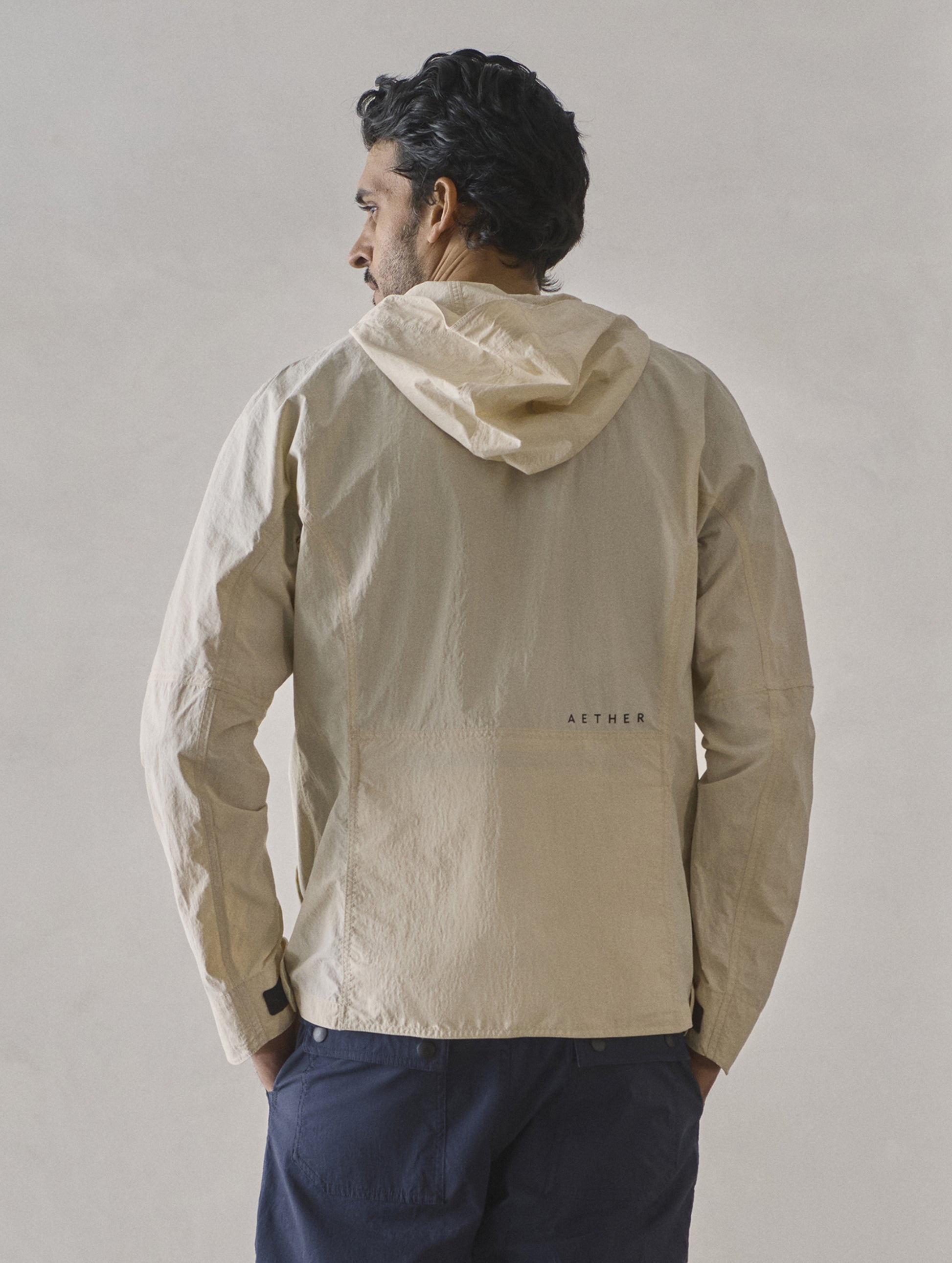 Rear view of man wearing Aires Lightweight Windbreaker in Bone white from AETHER Apparel.