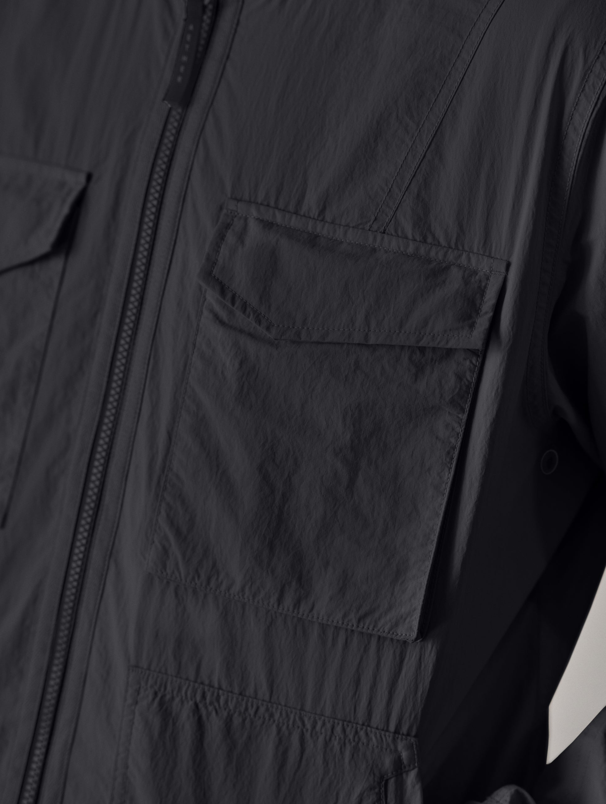 Closeup detailed view of the bottom of the main center-front zipper and the patch hand pockets on the Aires Lightweight Windbreaker in Onyx Black from AETHER Apparel.