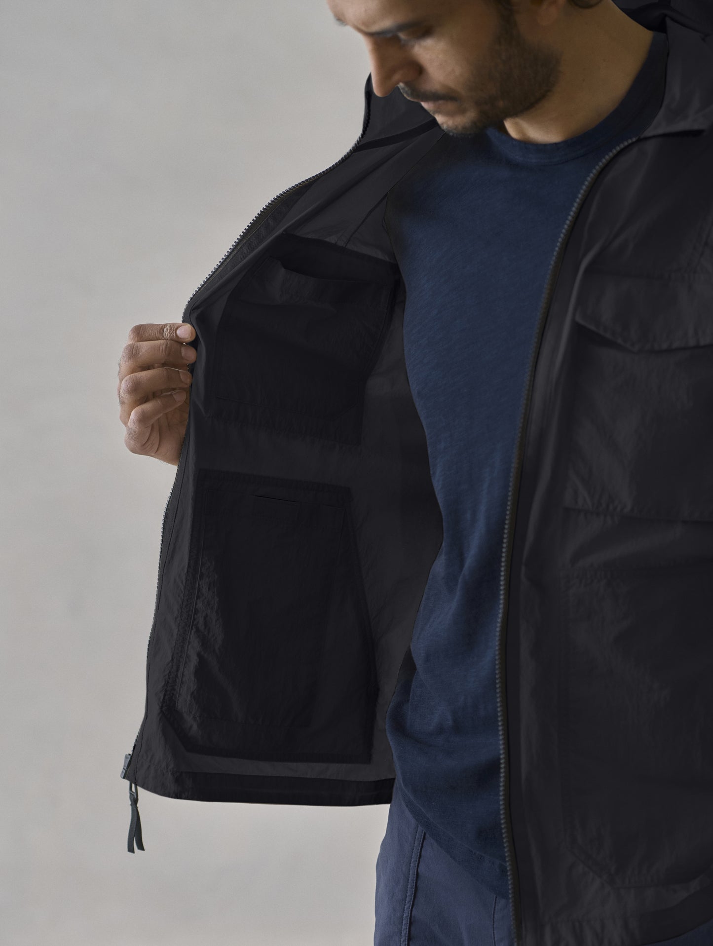 Studio image of man holding open the Aires Lightweight Windbreaker in Onyx Black from AETHER Apparel, showing off the interior pockets. 