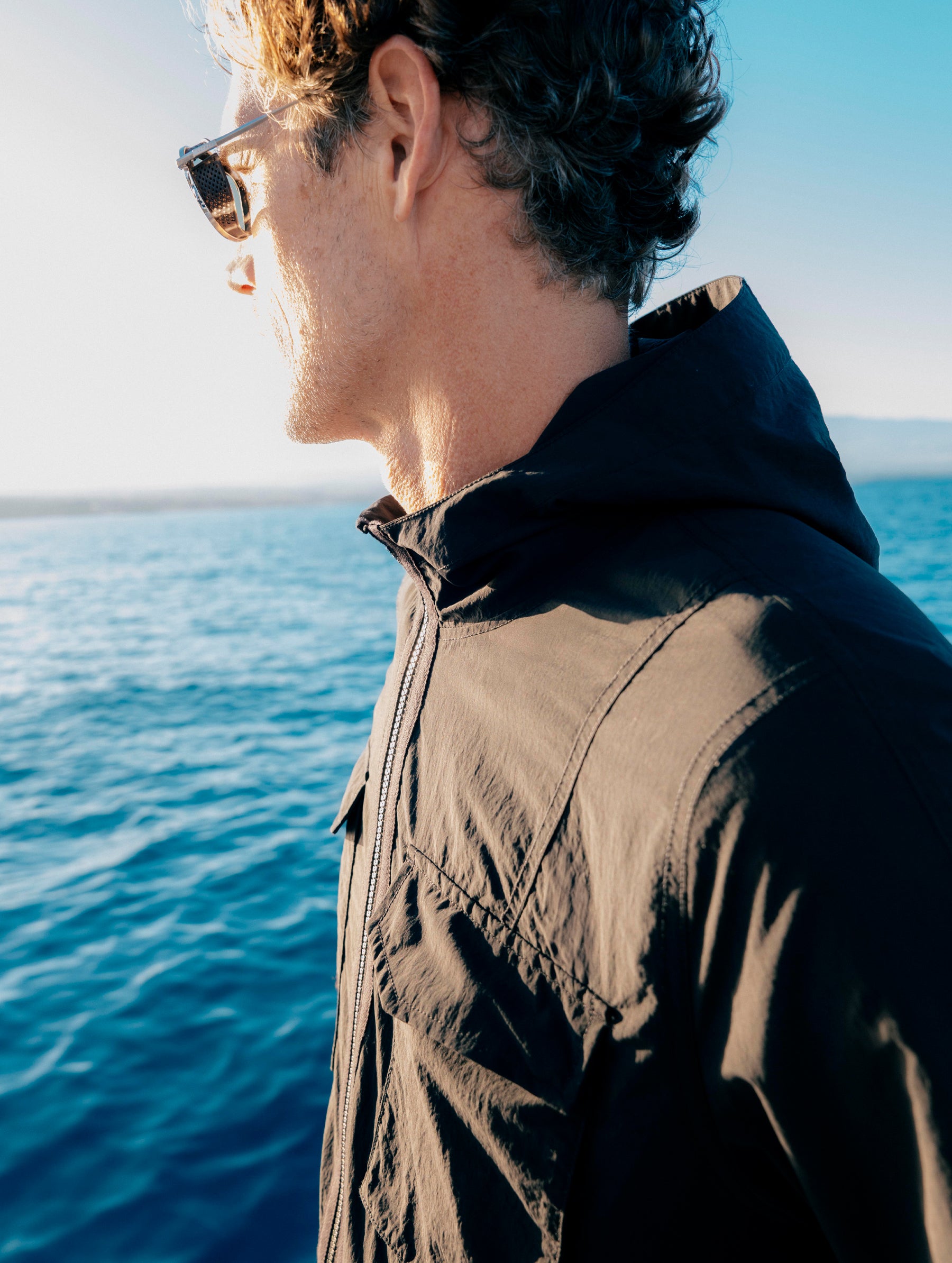 Lifestyle shot of main standing on a boat overlooking the ocean while wearing the Aires Lightweight Windbreaker in Onyx Black from AETHER Apparel.