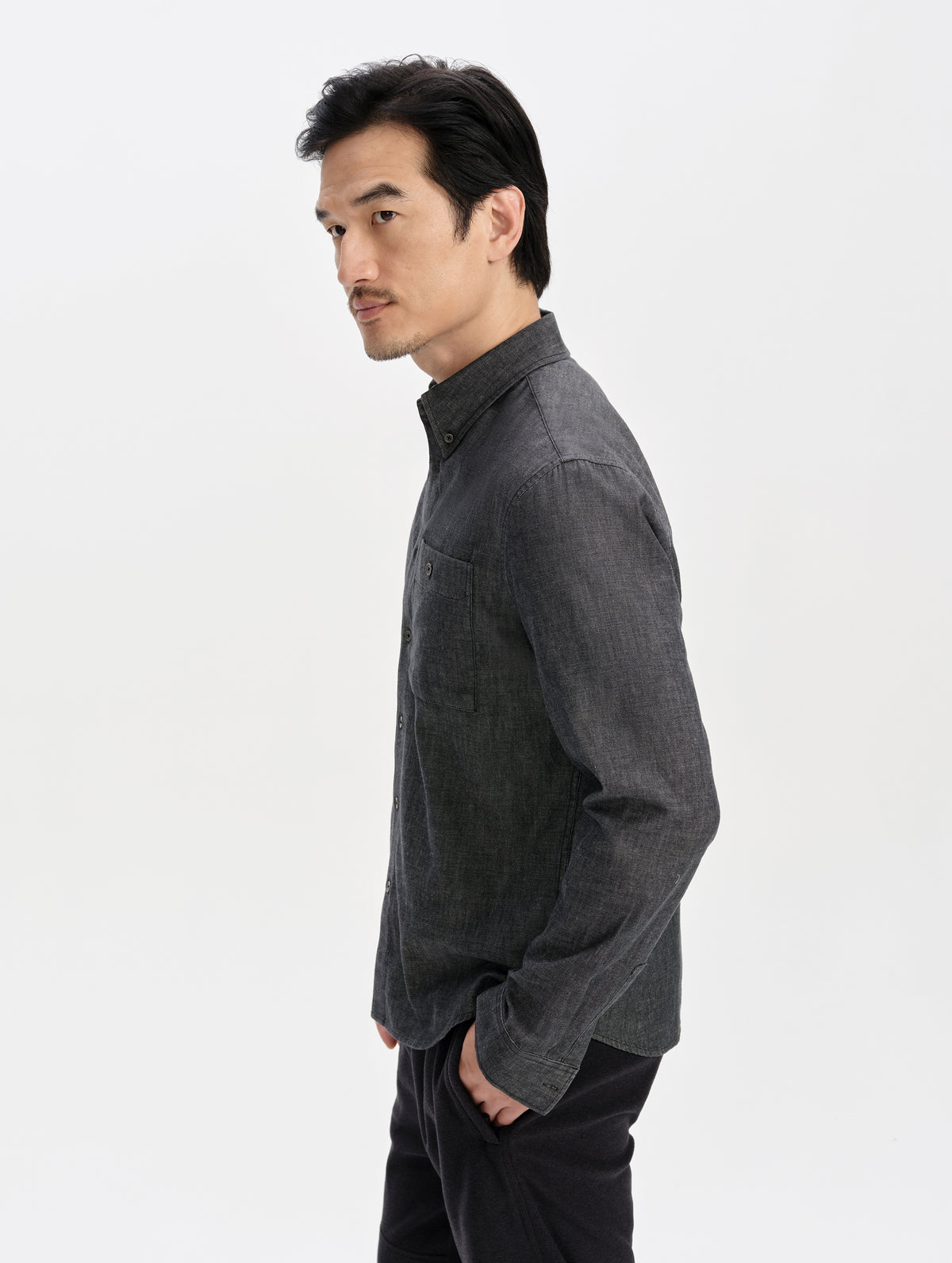 Side profile upper-body view of man wearing the Alder Chambray Button-Down in Black from AETHER Apparel.