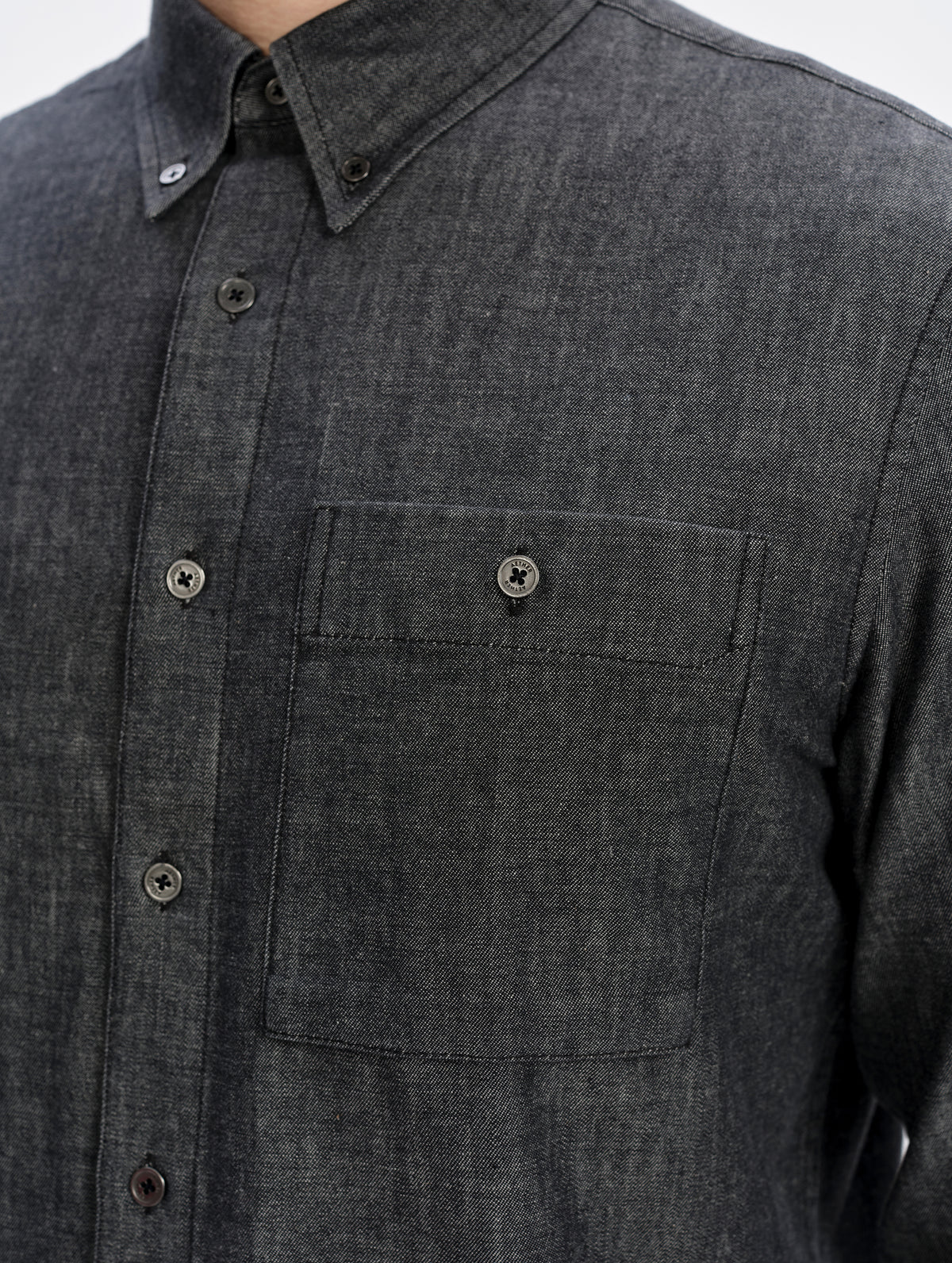 Closeup detailed view of the main center-front buttons and button-secured chest pocket on the Alder Chambray Button-Down in Black from AETHER Apparel.