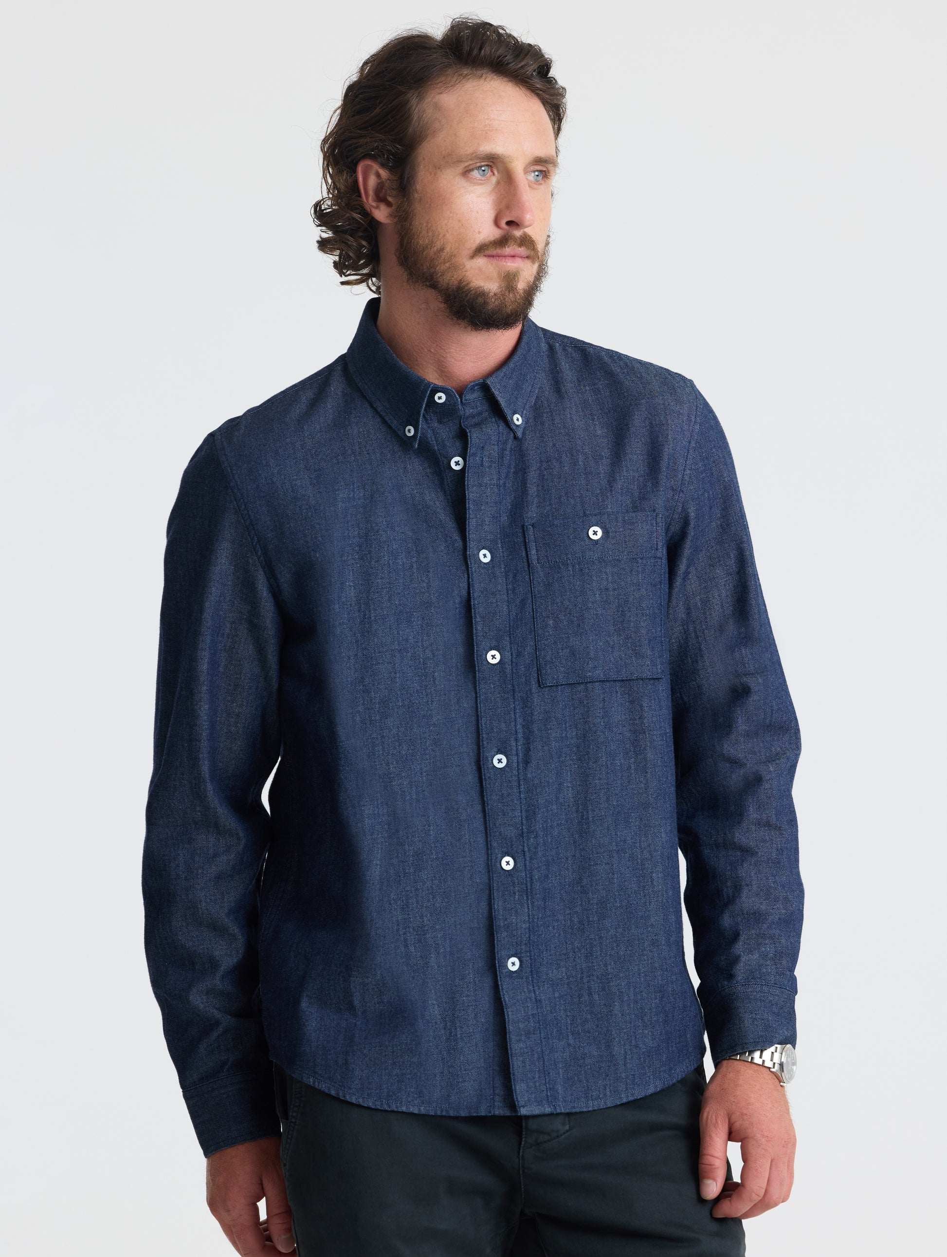 Angled view of man wearing Alder Chambray Button-Down in Dark Blue from AETHER Apparel.