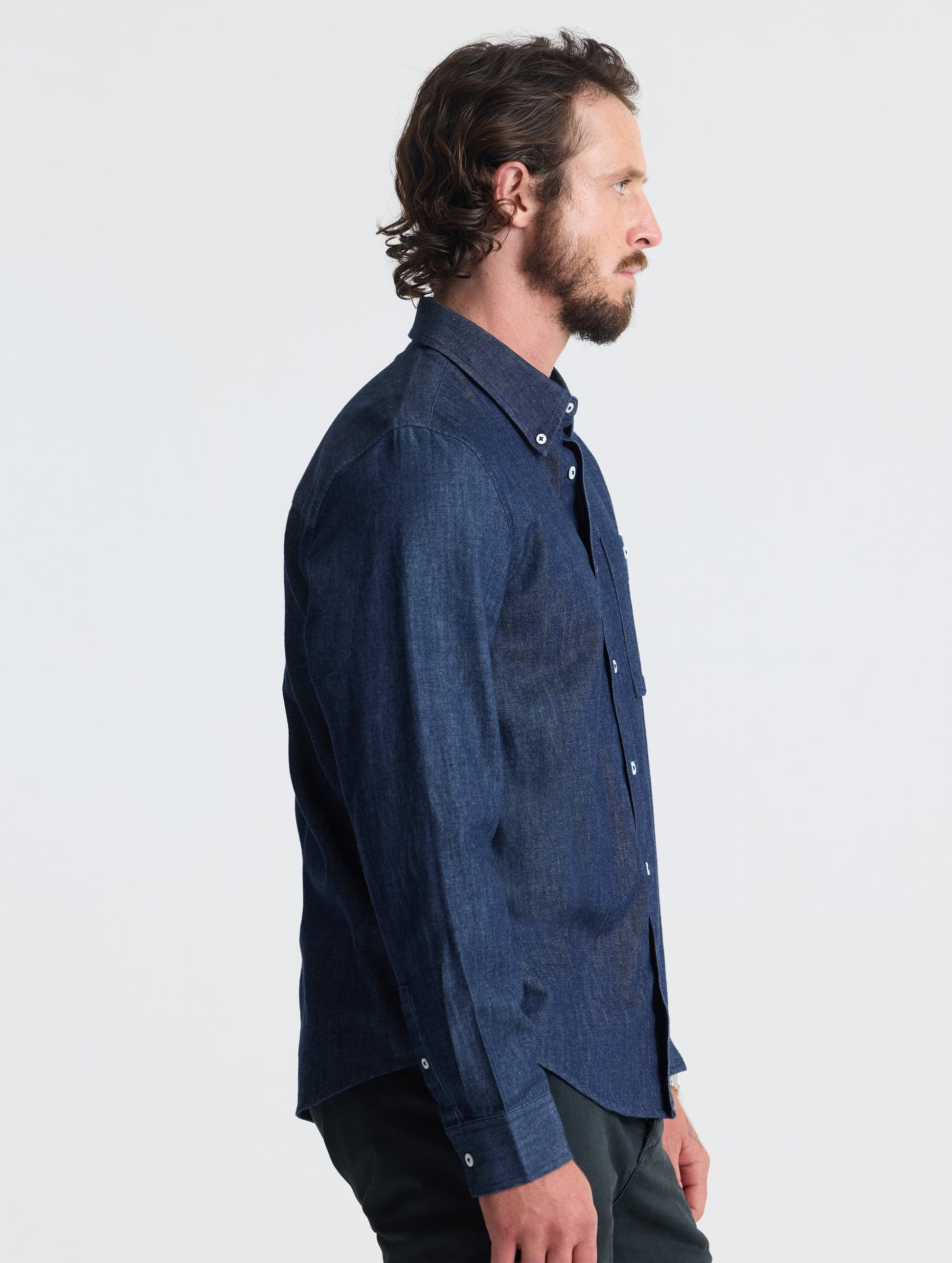 Side profile of man wearing Alder Chambray Button-Down in Dark Blue from AETHER Apparel.