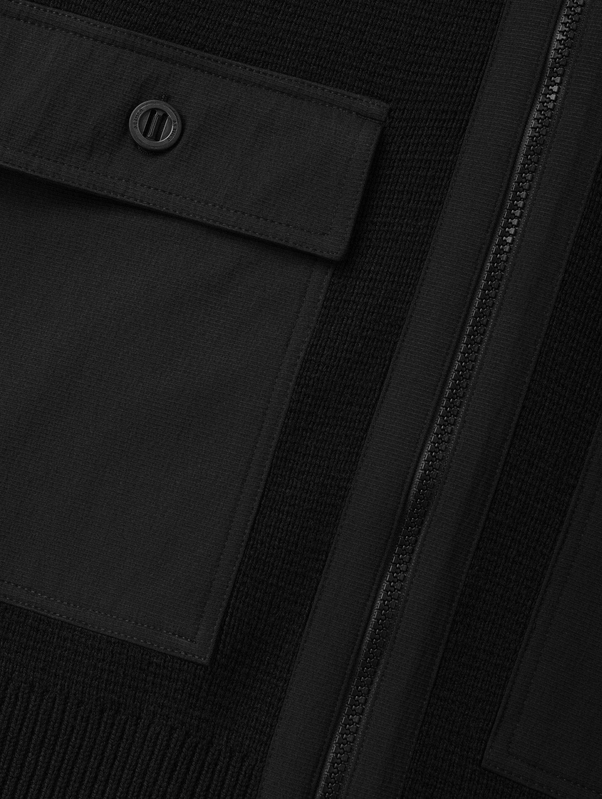 Closeup detailed view of the main center-front zipper and chest patch pockets on the Benson Full-Zip Sweater in Onyx Black from AETHER Apparel.