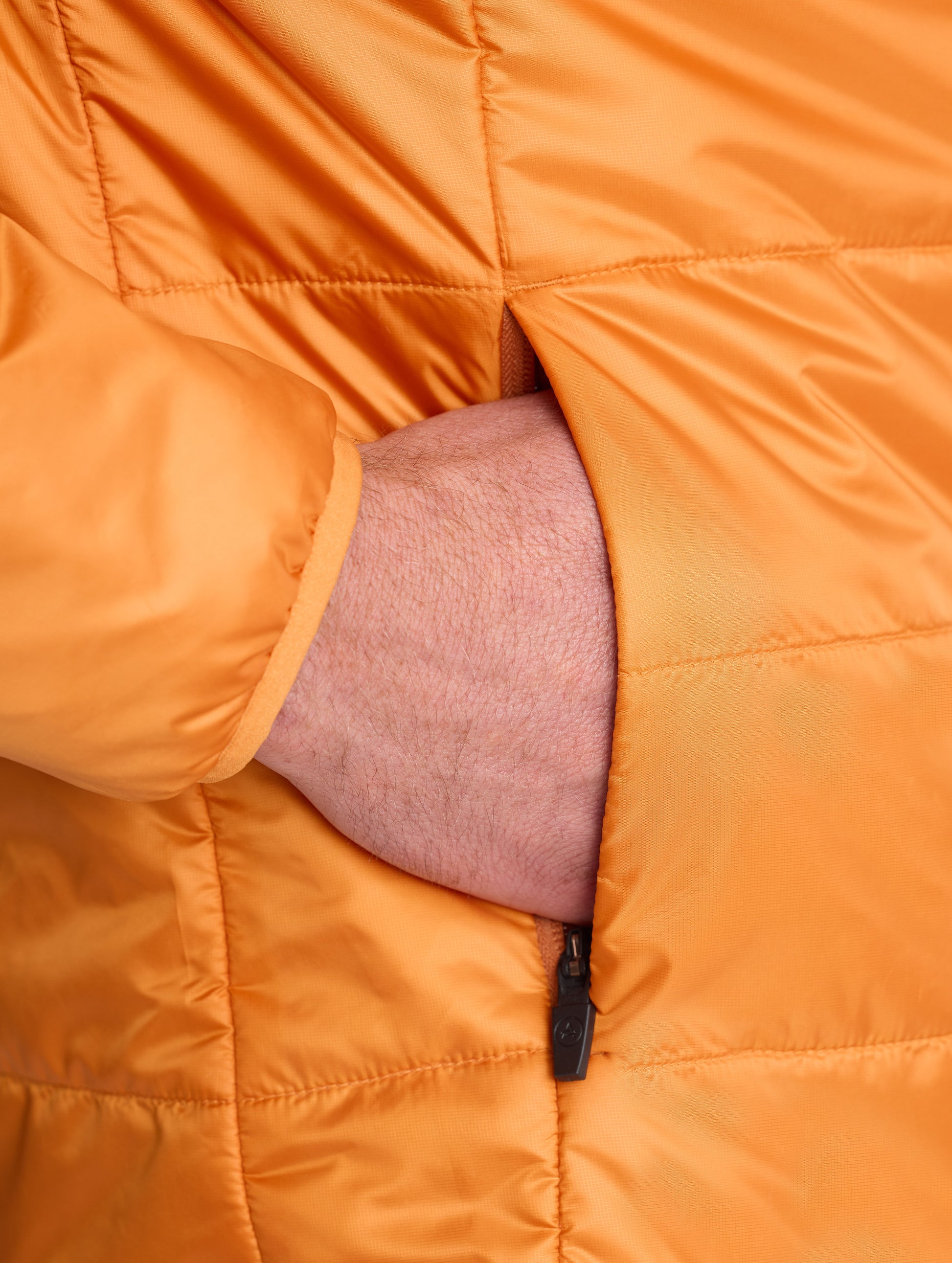 Closeup view of wearer's hand in right pocket of Eco Insulated Jacket in Autumn Orange from AETHER Apparel.