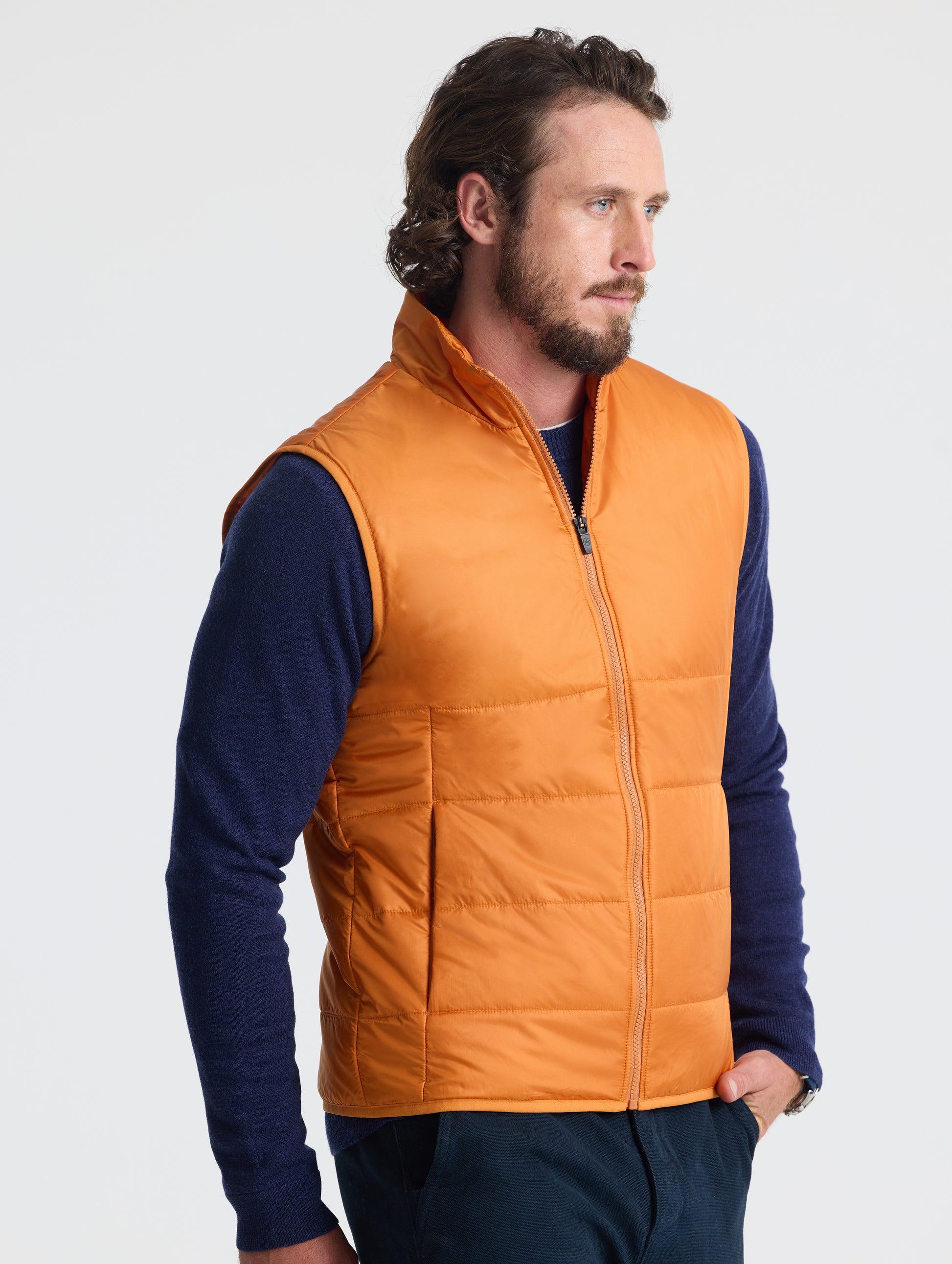 Angled view of man wearing Eco Insulated Vest in Autumn Orange from AETHER Apparel.