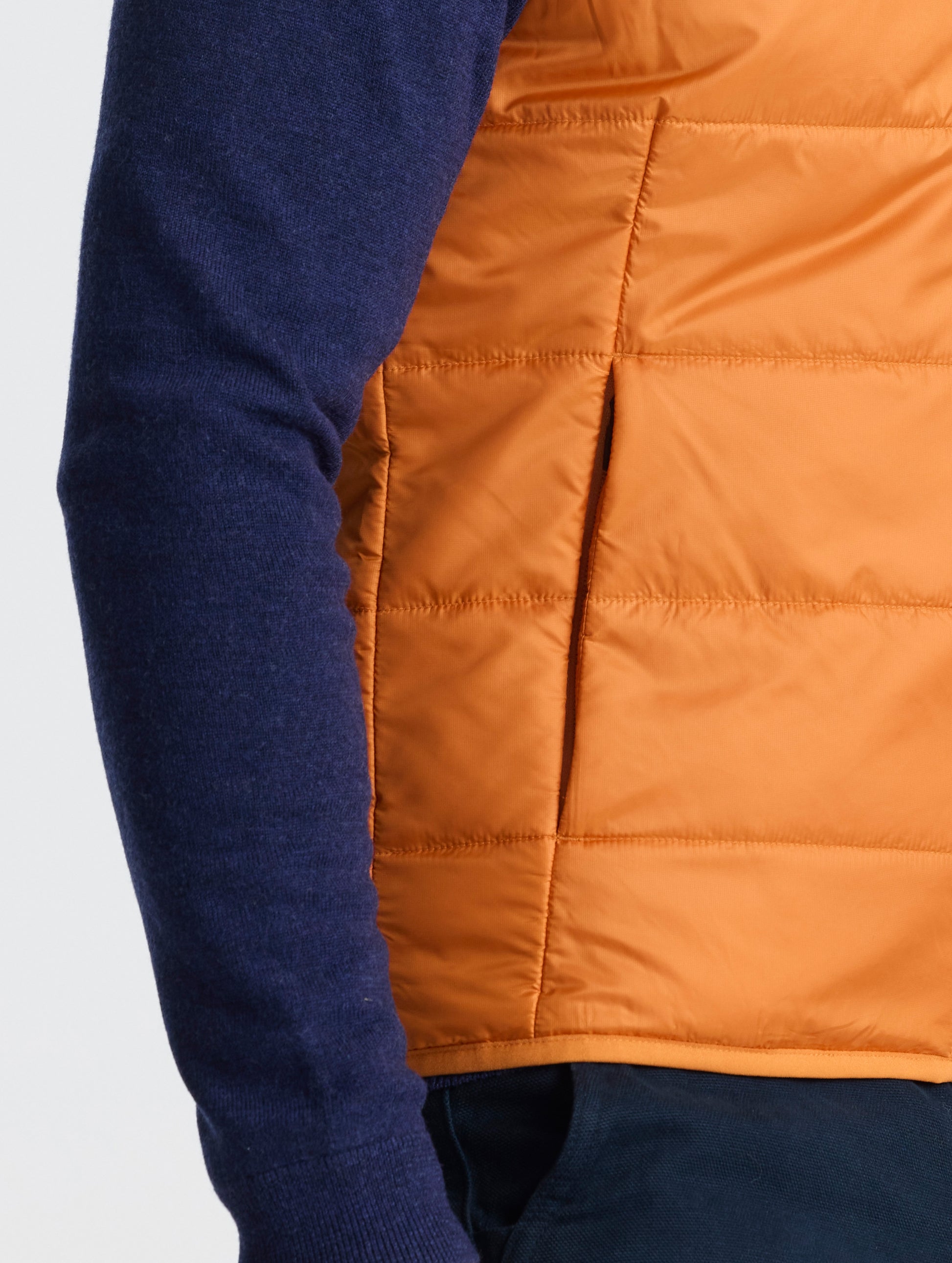 Closeup view of wearer's right hand pocket of Eco Insulated Vest in Autumn Orange from AETHER Apparel.