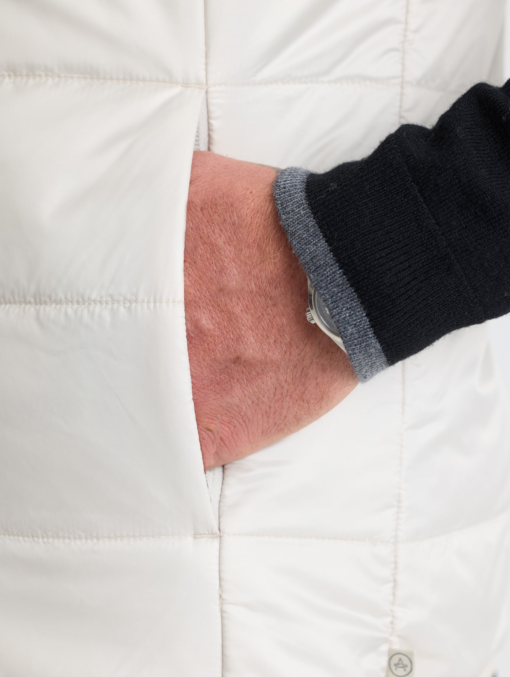 Closeup view of wearer's hand in left hand pocket of Eco Insulated Vest in Bone white from AETHER Apparel.
