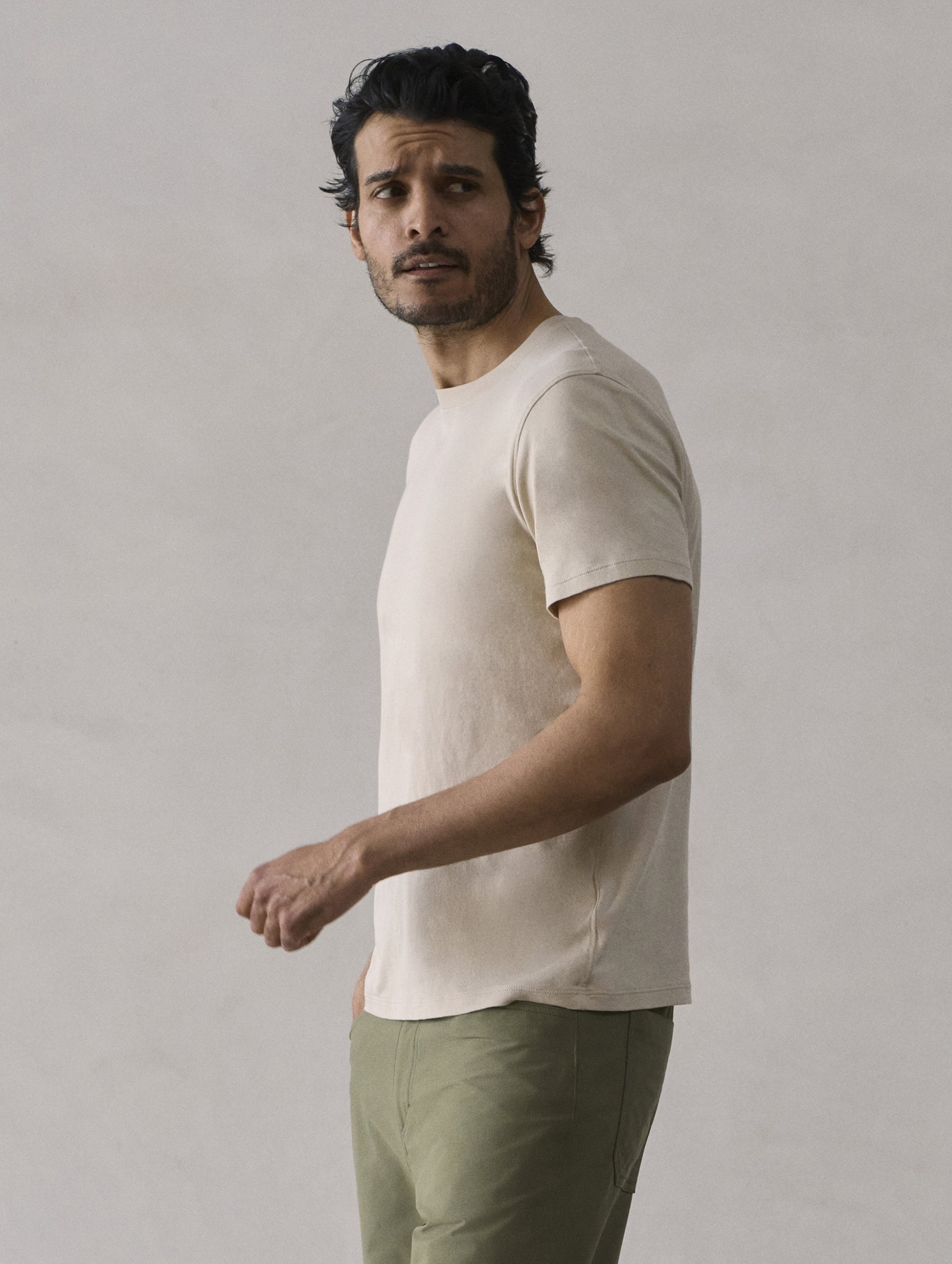 Side profile view of man wearing Emery Pima Crew Tee in Bone white from AETHER Apparel.