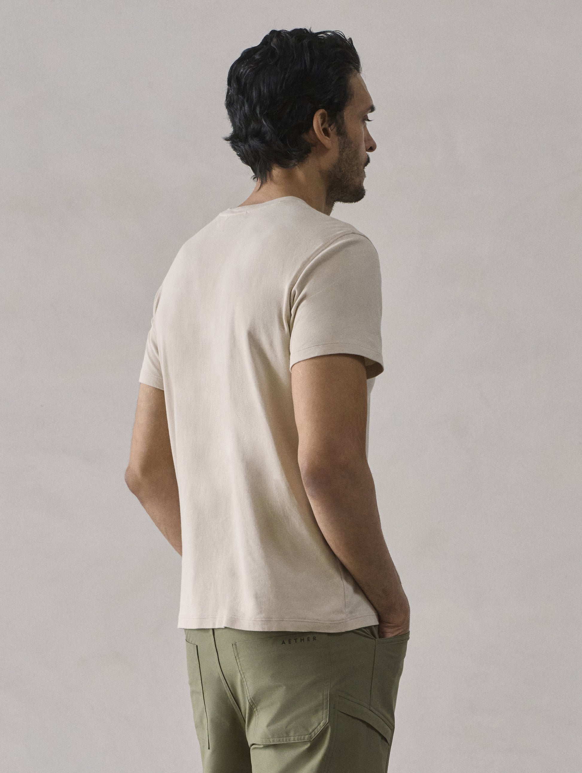 Rear 3/4 view of man wearing Emery Pima Crew Tee in Bone white from AETHER Apparel.