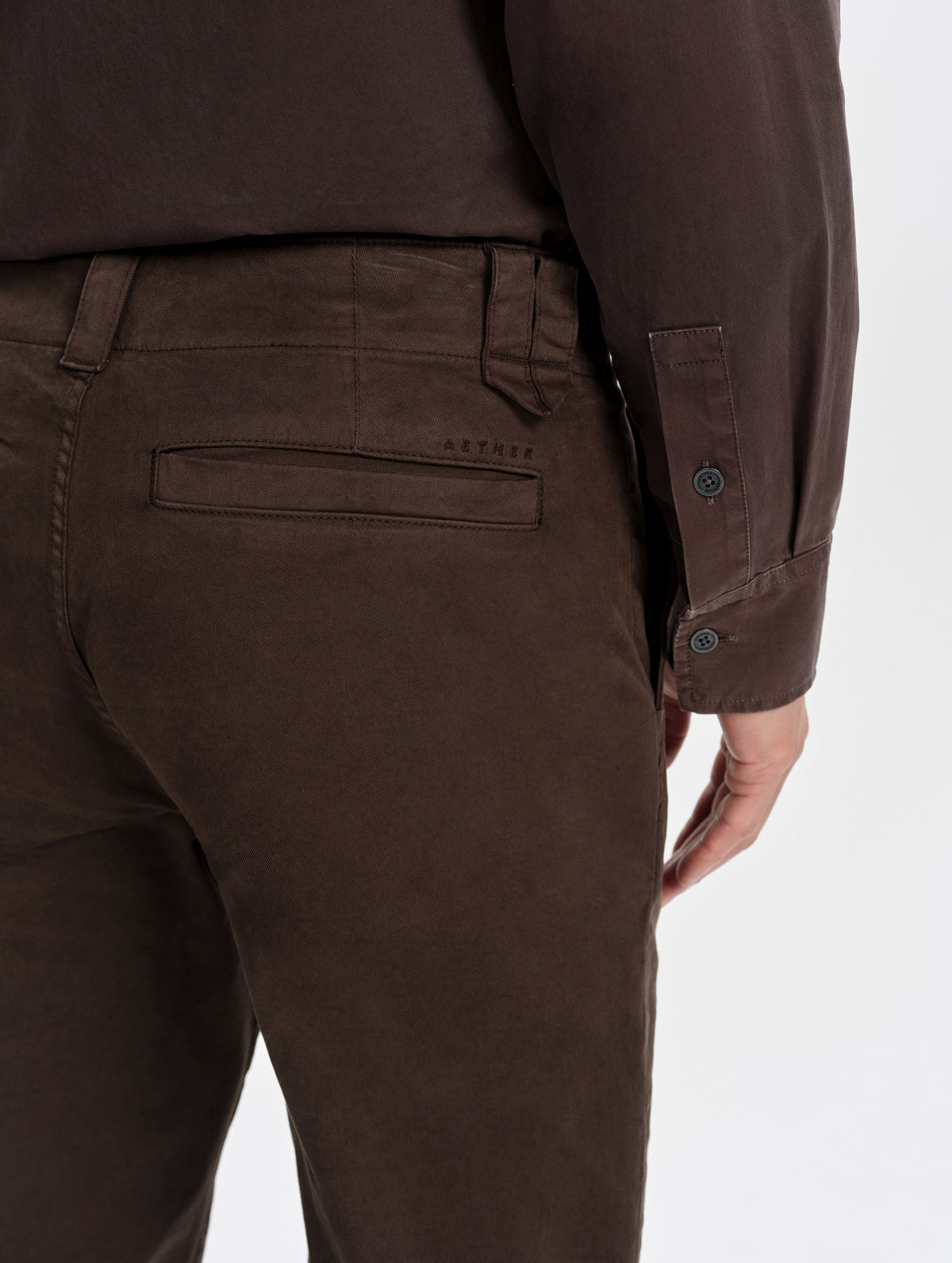 Closeup detailed view of the embroidered AETHER wordmark and welt back pockets on the Flint Chino Pant in Ash Brown from AETHER Apparel.