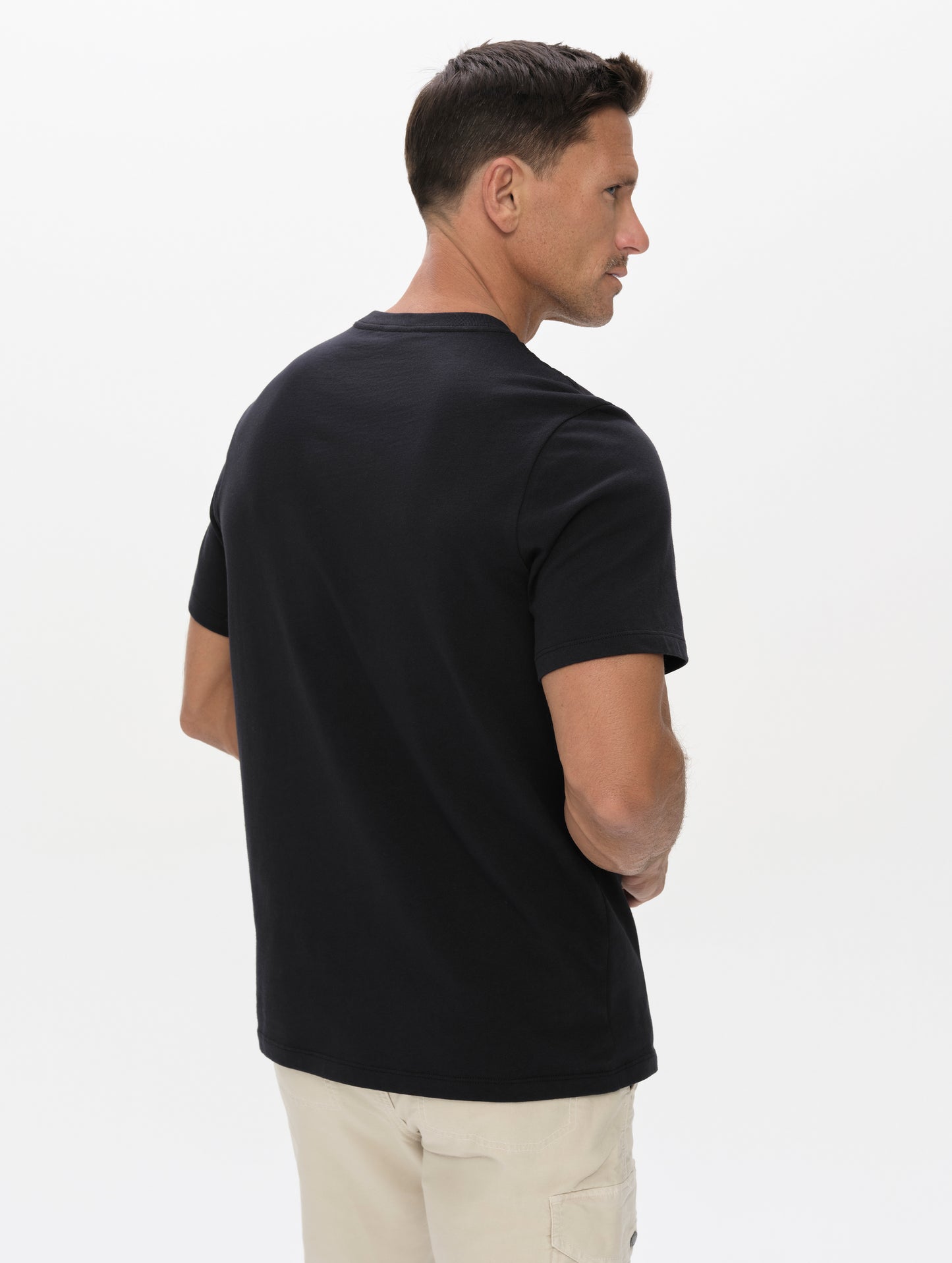 Rear, angled upper-body view of man wearing the Graphic Tee AETHER Logo in Onyx Black from AETHER Apparel.