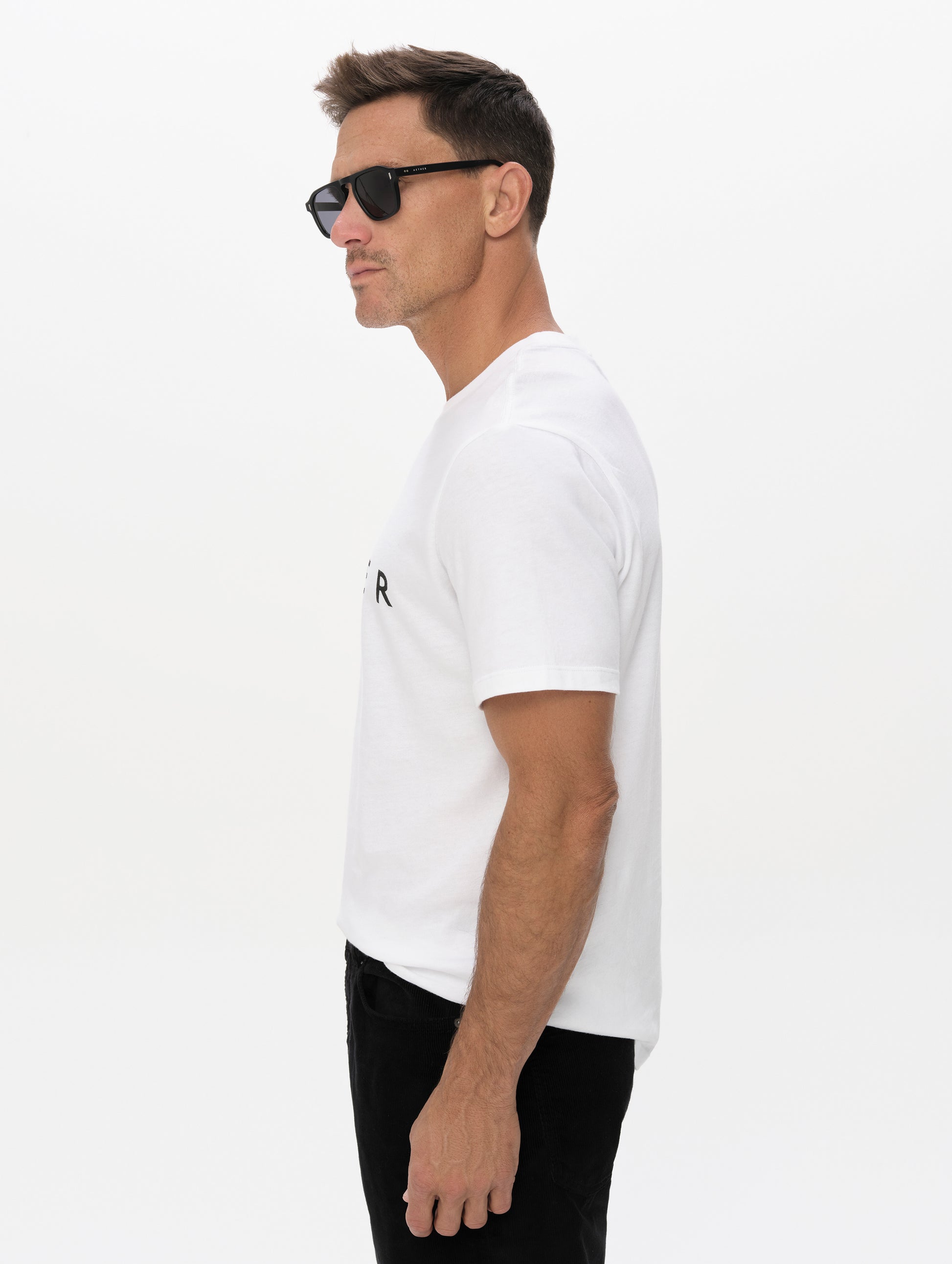 Side, profile, upper-body view of man wearing the Graphic Tee AETHER Logo in White from AETHER Apparel.