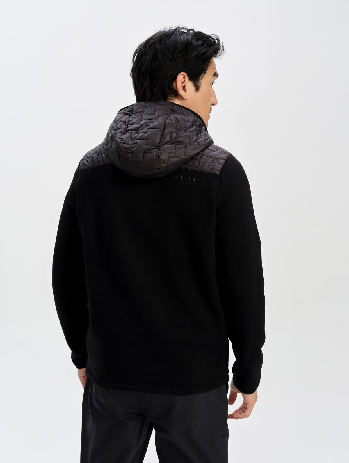 Rear upper-body view of man wearing the Hybrid Tech Full-Zip 2.0 in Onyx Black from AETHER Apparel. 