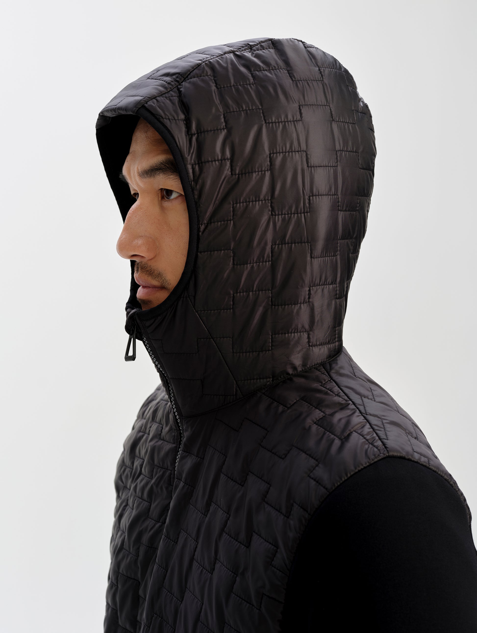 Side profile view of man with hood up wearing the Hybrid Tech Anorak in Onyx Black from AETHER Apparel. 