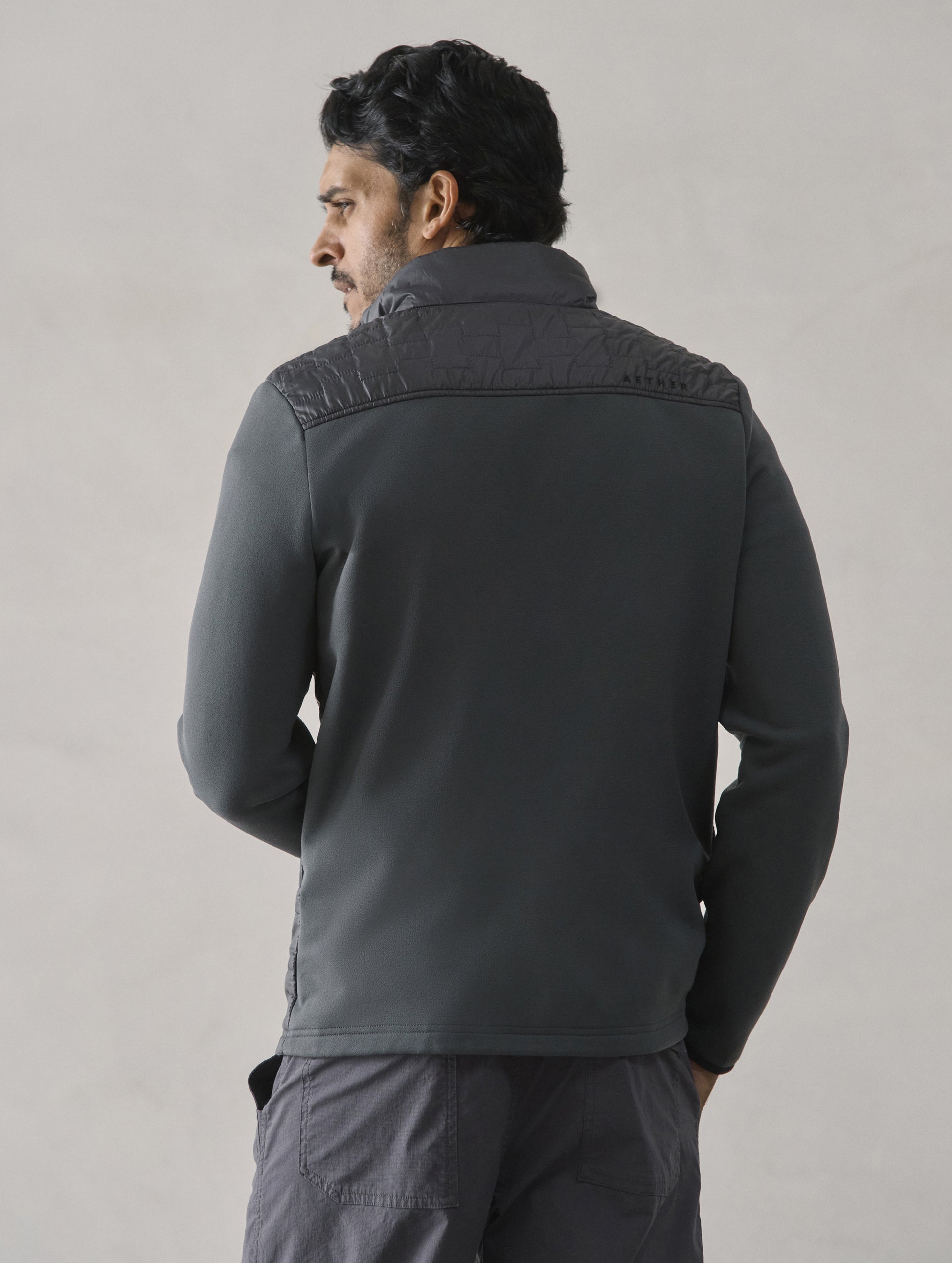 Rear view of man wearing Hybrid Tech Full-Zip in Graphite from AETHER Apparel.