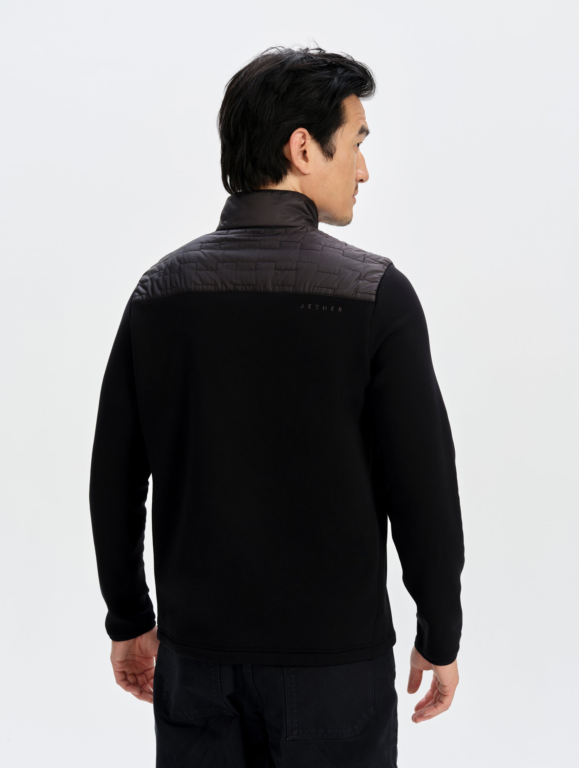 Rear upper-body view of man wearing the Hybrid Tech Full-Zip 2.0 in Onyx Black from AETHER Apparel. 
