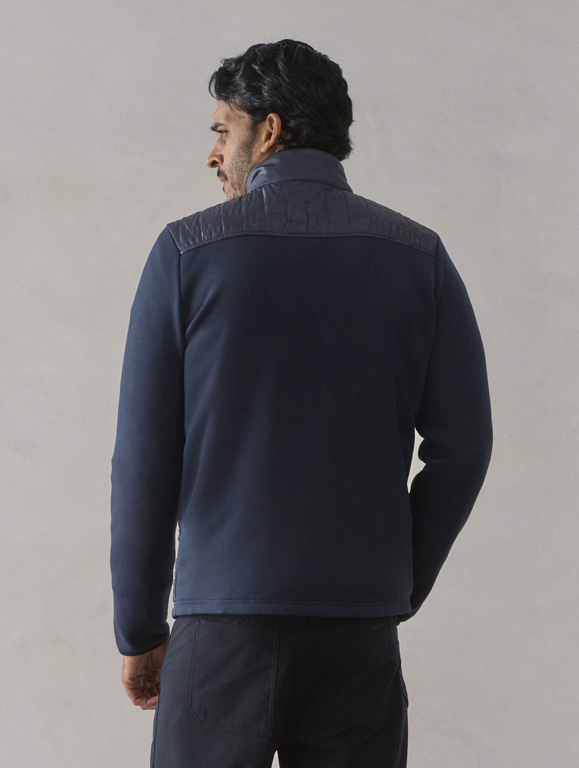 Rear view of man wearing Hybrid Tech Full-Zip in Total Eclipse dark blue from AETHER Apparel.