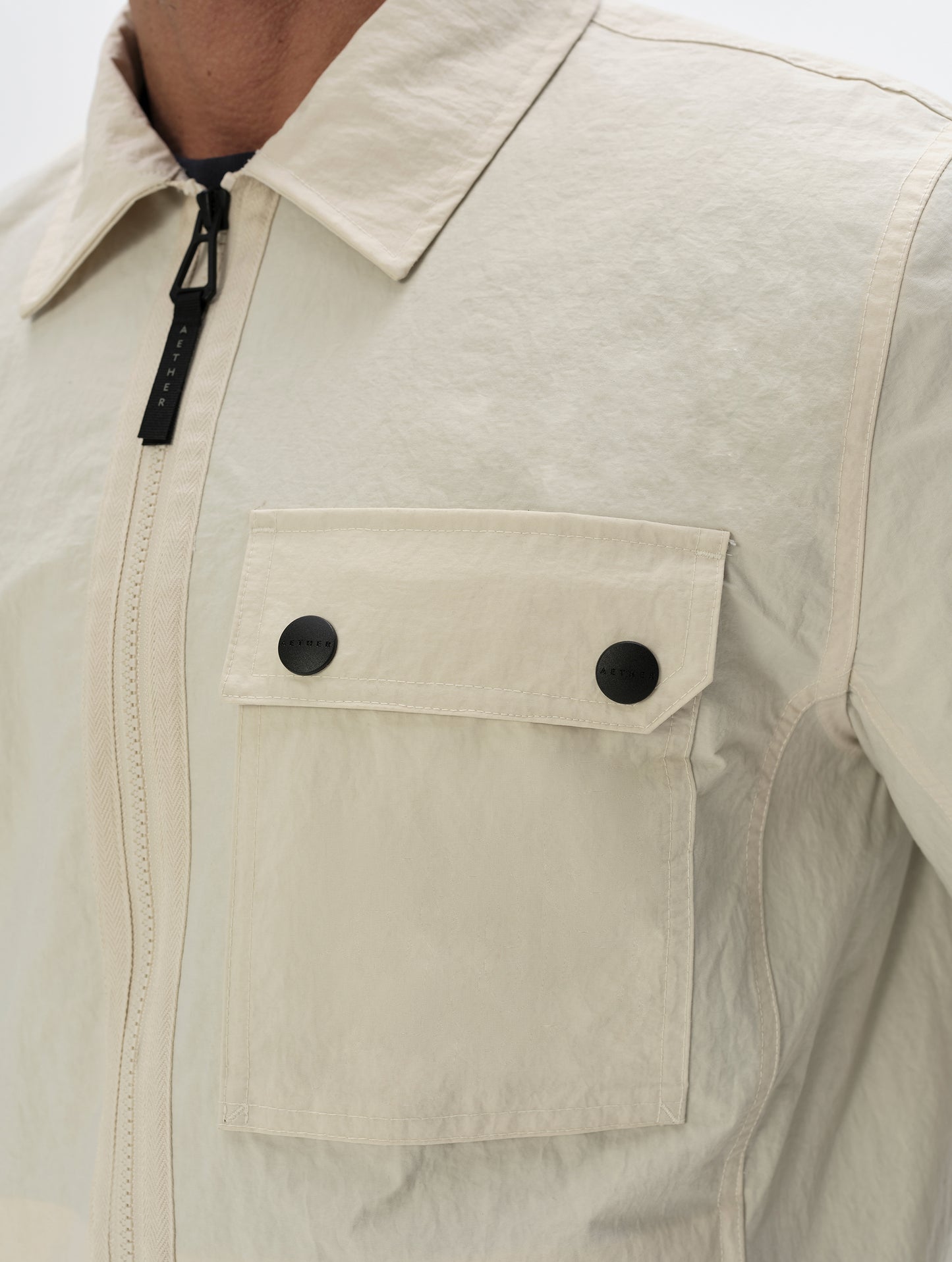 Closeup detailed view of the center-front zipper, collar, and dual-button chest pocket on the Landon Jacket in Bone from AETHER Apparel.