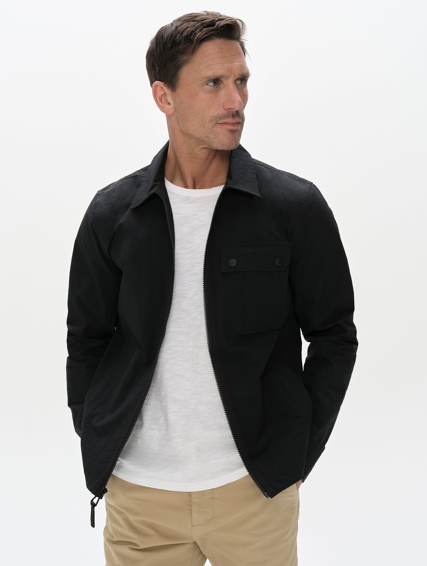 Front, upper-body view of man wearing the Landon Jacket in Onyx Black from AETHER Apparel unzipped. 