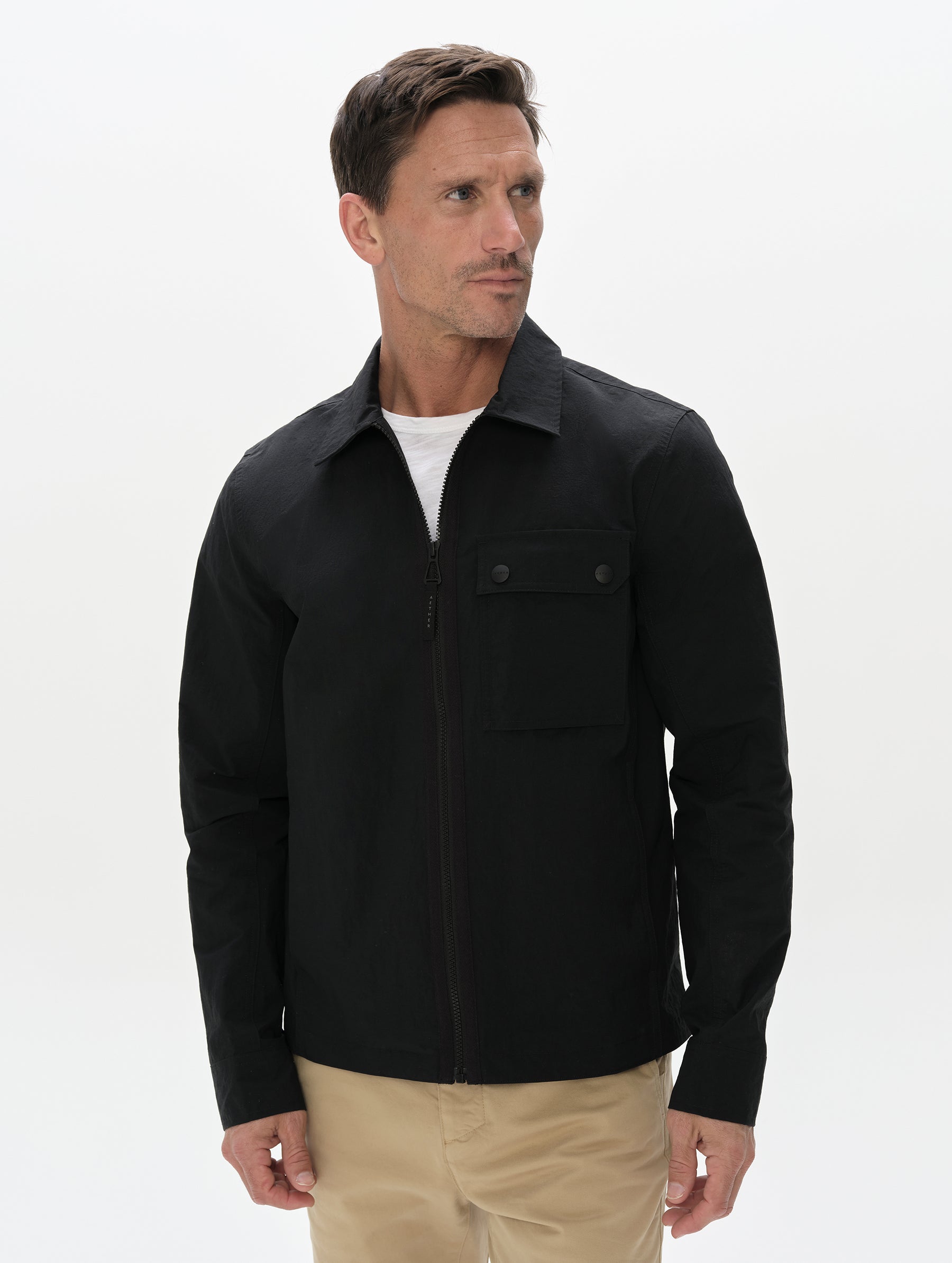 Front, upper-body view of man wearing the Landon Jacket in Onyx Black from AETHER Apparel zipped up.