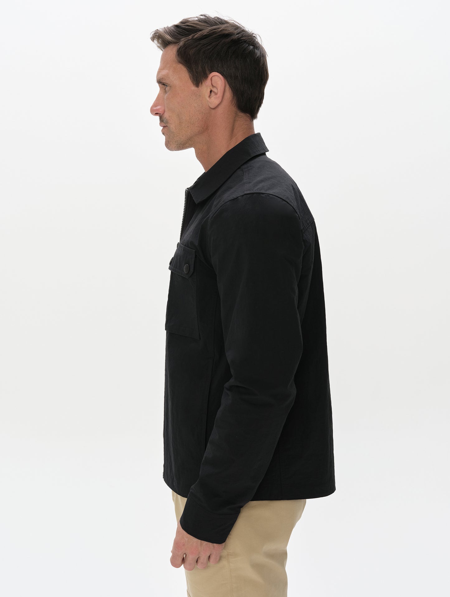 Side profile, upper-body view of man wearing the Landon Jacket in Onyx Black from AETHER Apparel unzipped. 