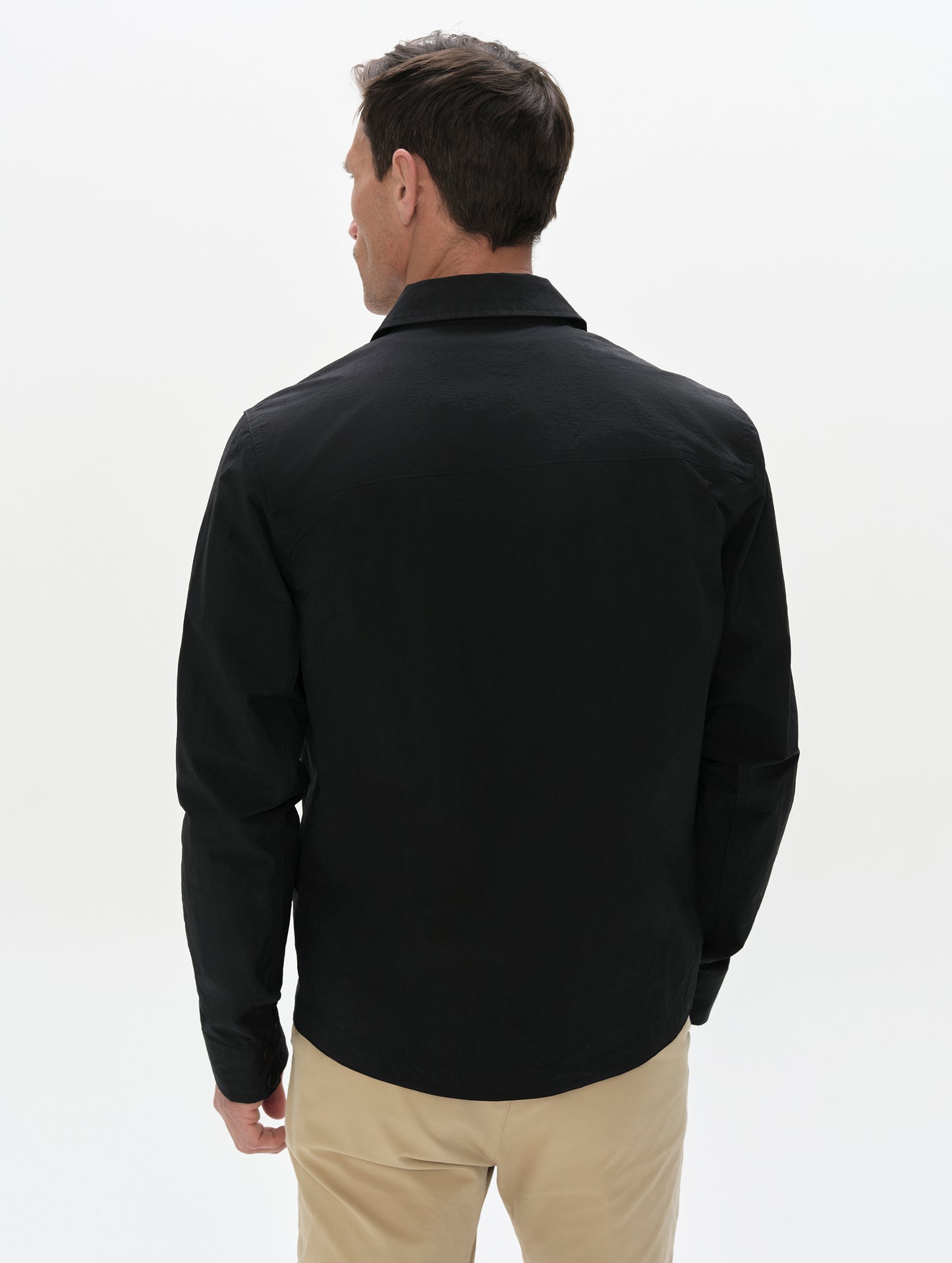 Rear, upper-body view of man wearing the Landon Jacket in Onyx Black from AETHER Apparel unzipped. 